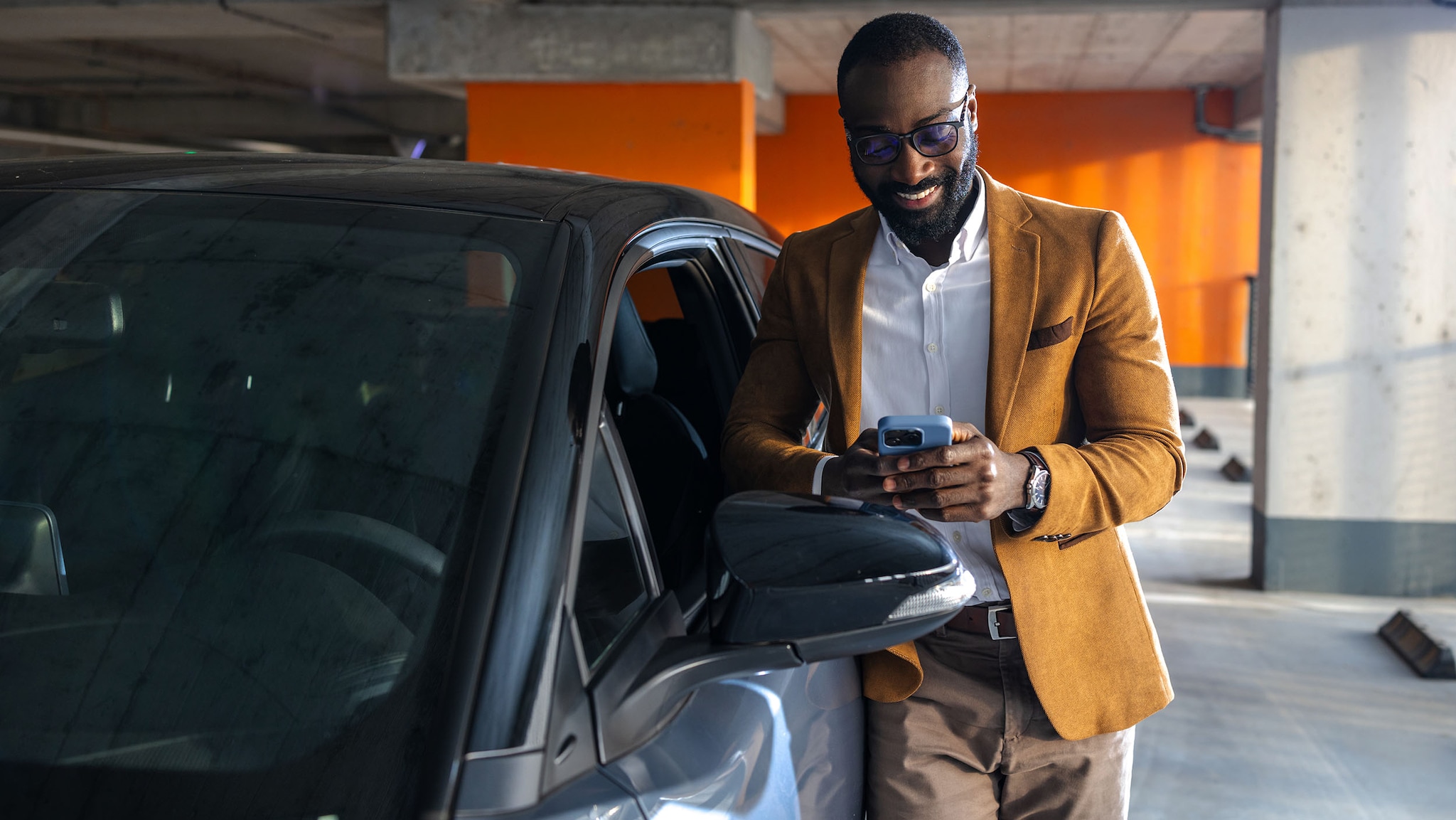 Ein Mann lehnt an einem Auto und schaut auf sein Smartphone.