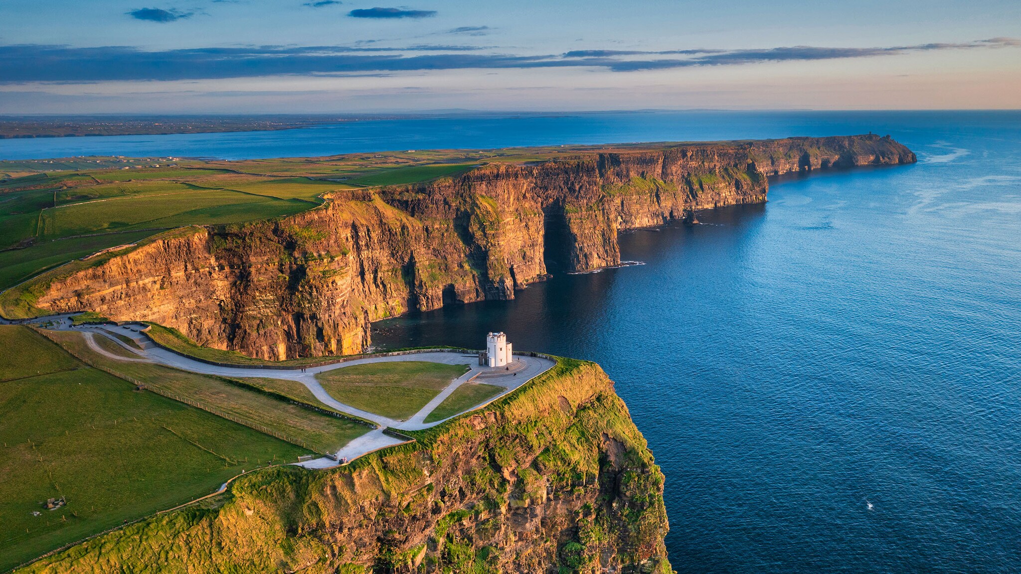Eine Küste mit grüner Wiese und roten Klippen liegt am Meer.