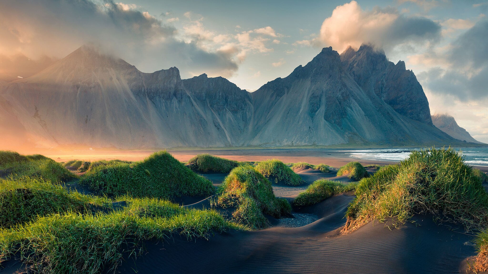 Hinter einer grünen Wiese liegt eine Berglandschaft.