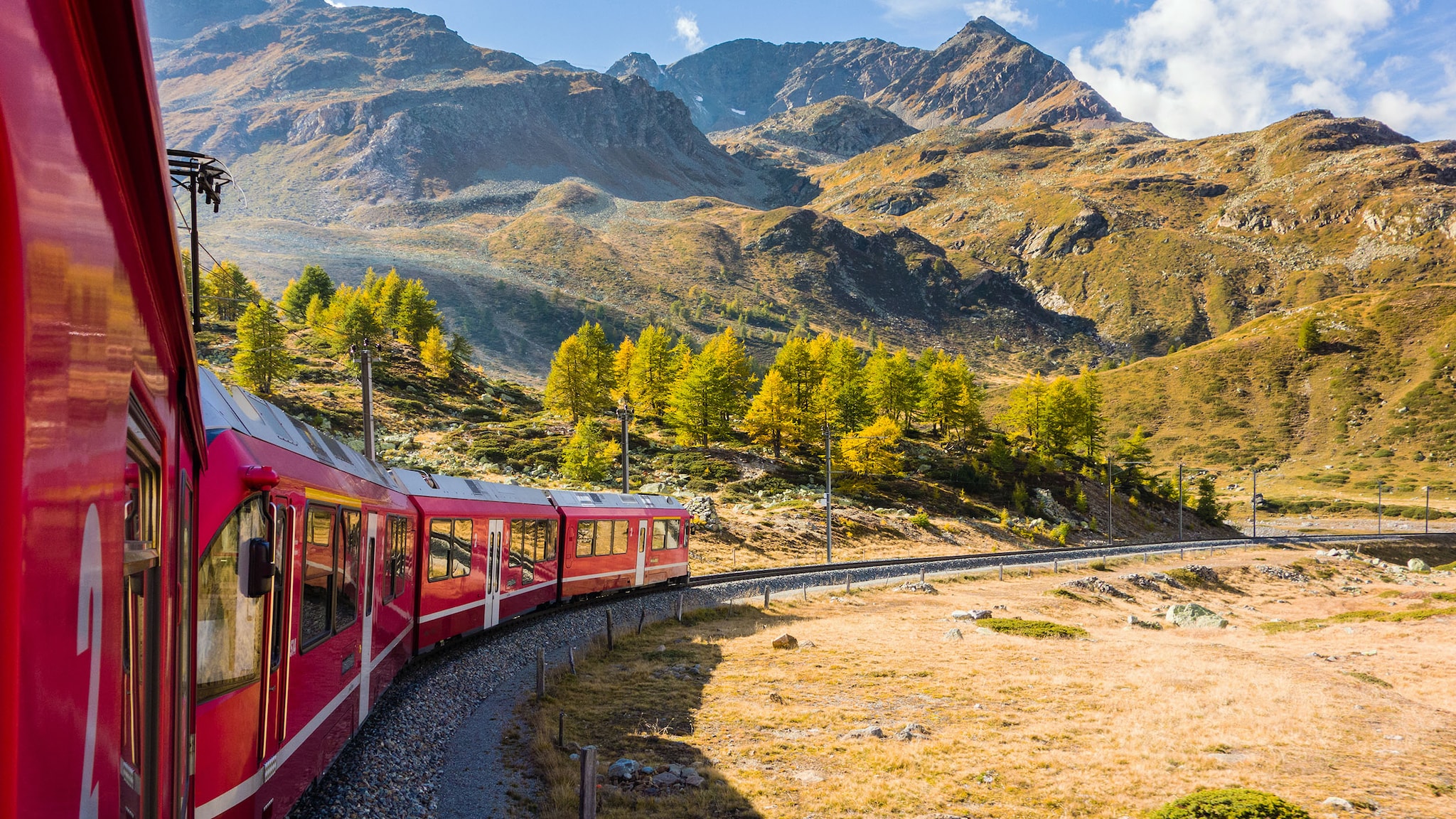 Ein roter Zug fährt vor einer Berglandschaft entlang.