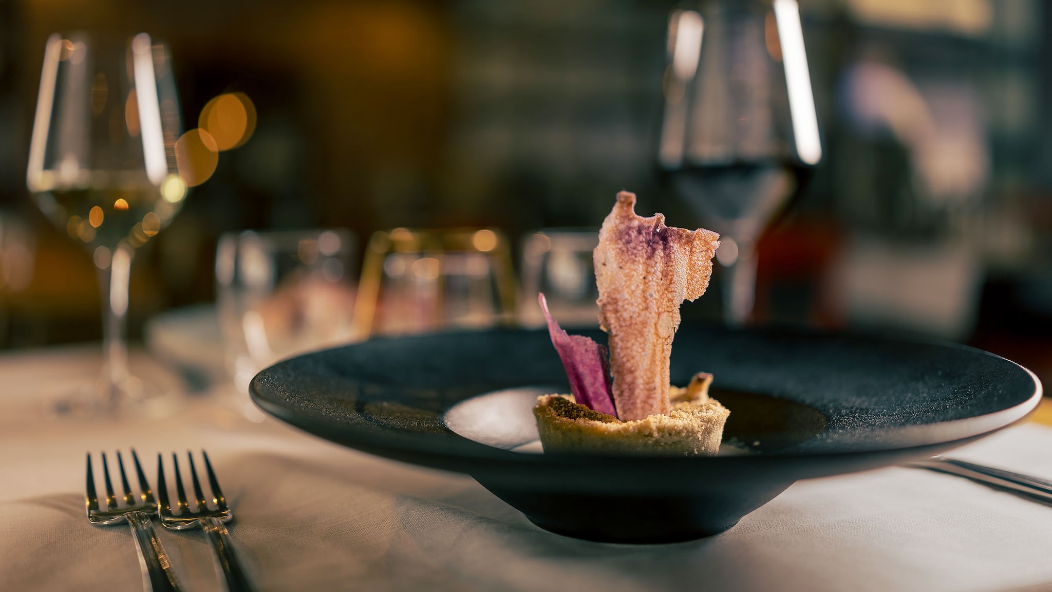 Eine kunstvoll angerichtete Vorspeise auf einem schwarzen Teller auf einem elegant gedeckten Tisch.