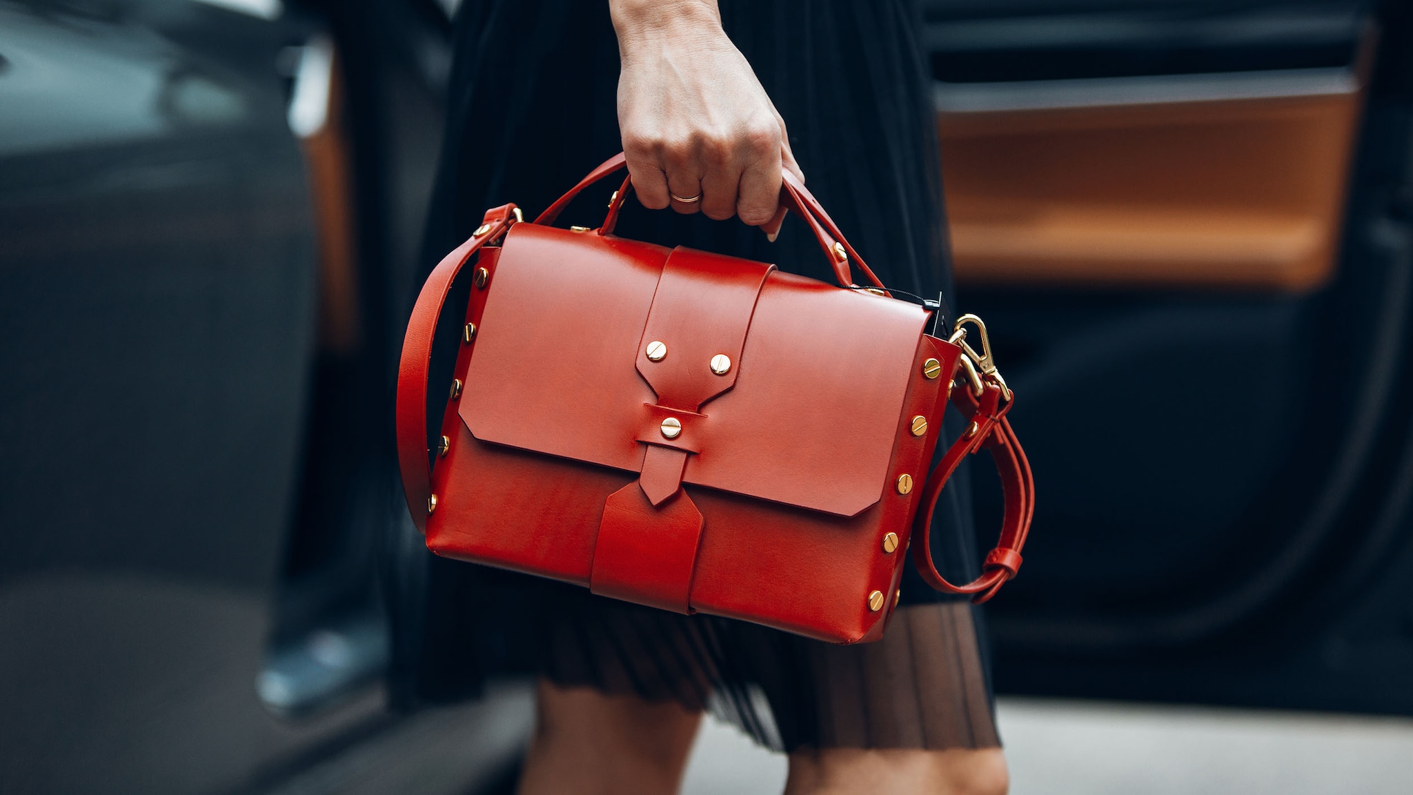 Nahaufnahme einer roten Lederhandtasche mit Nieten in der Hand einer Frau im schwarzen Kleid.
