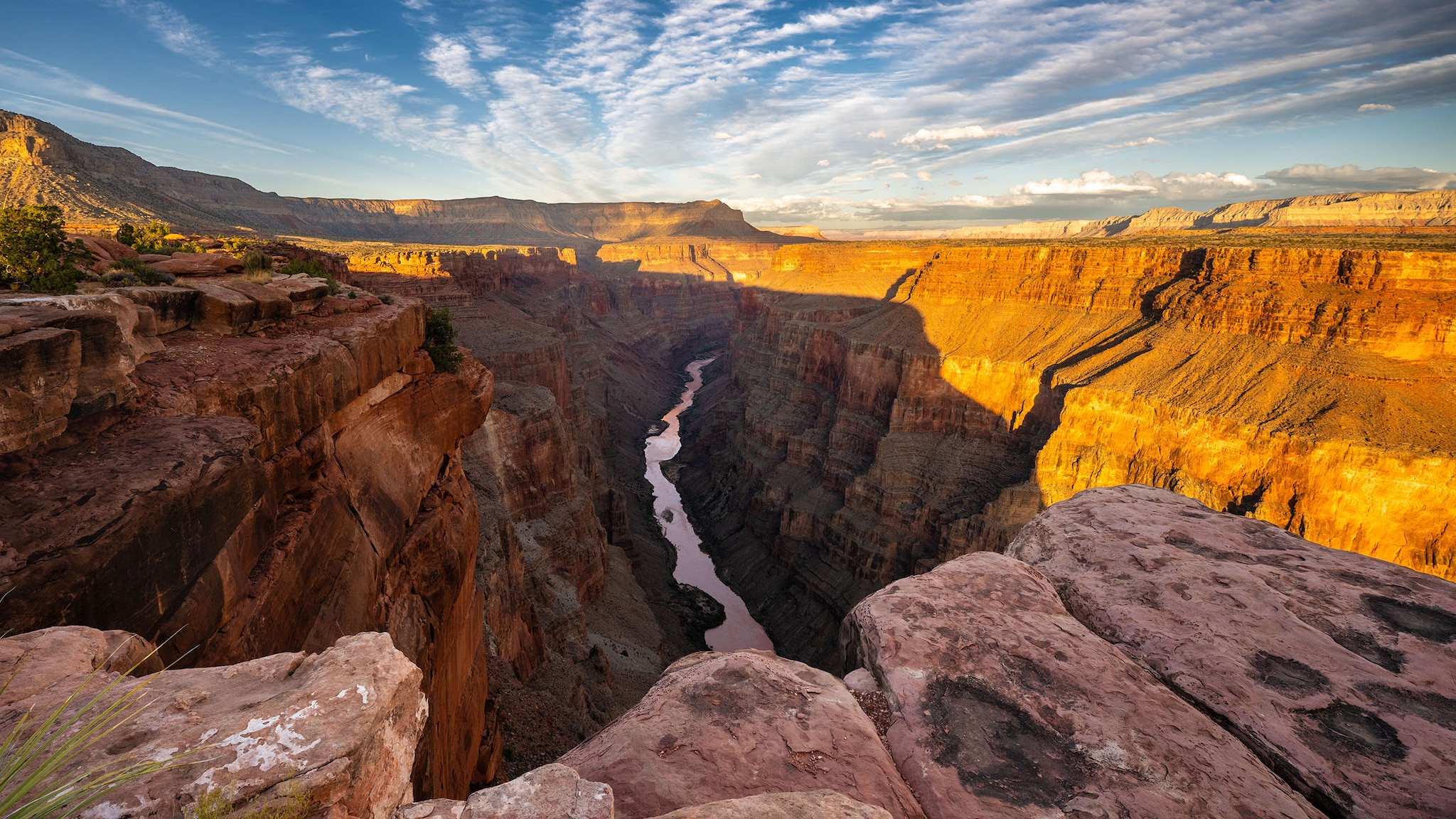 Panoramaaufnahme eines großen Canyons mit Schluchten-Bach, halb in goldenes Sonnenlicht getaucht.