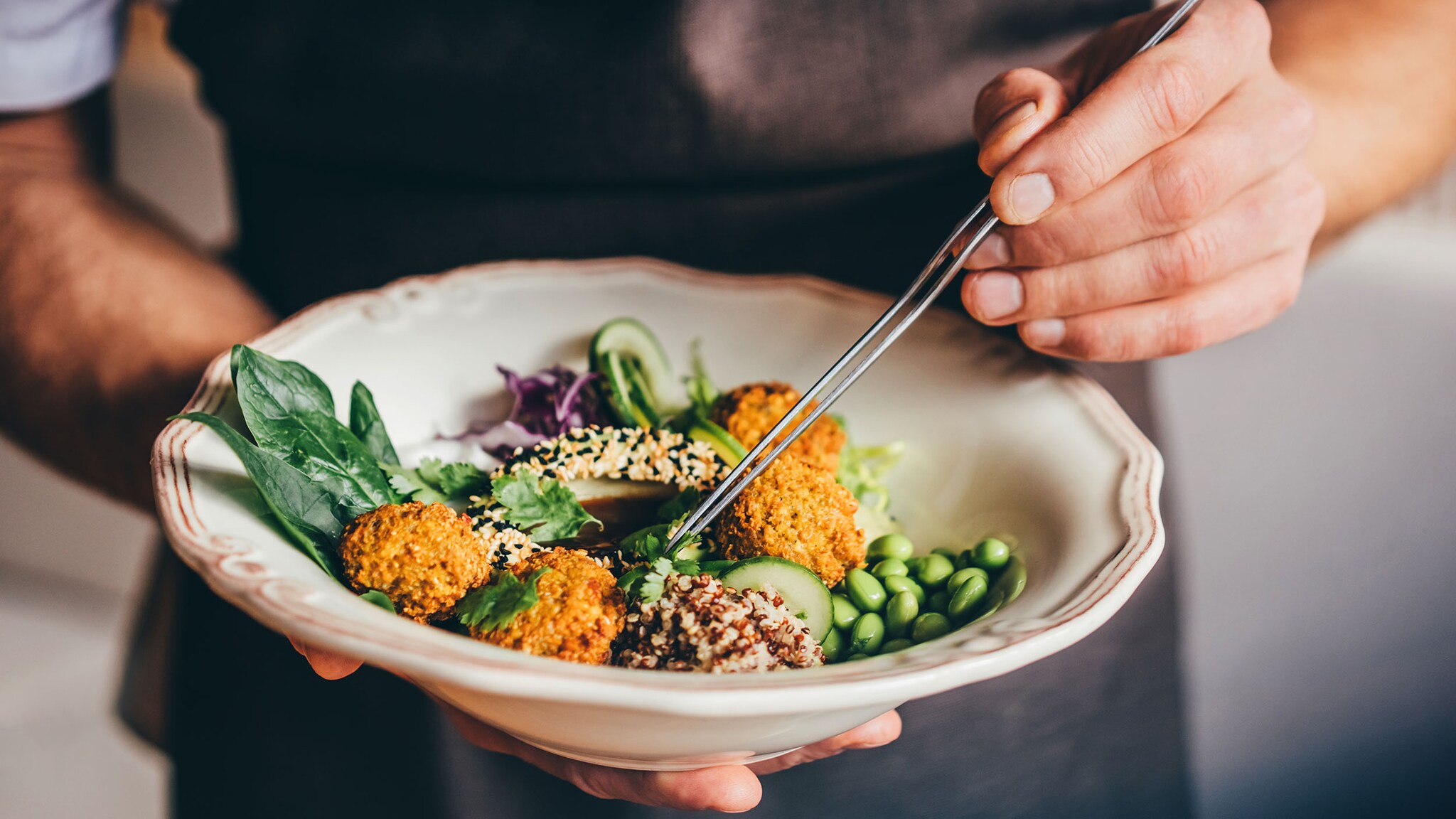 Ein Mann hält einen Teller mit Gemüse und Falafel in der Hand.