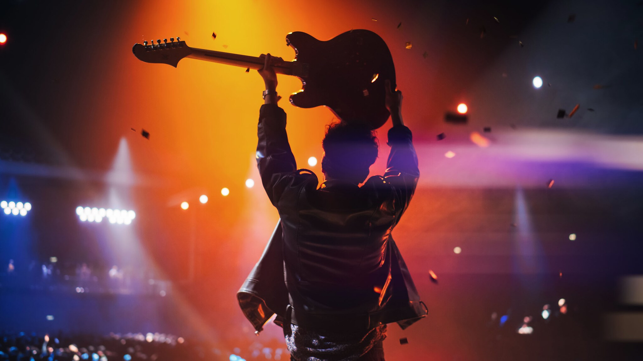 Ein Mann steht auf der Bühne und hält eine Gitarre über dem Kopf.