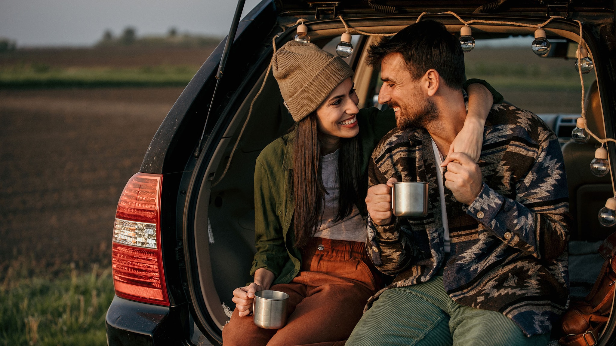 Ein Paar sitzt mit Bechern im Kofferraum eines Autos.