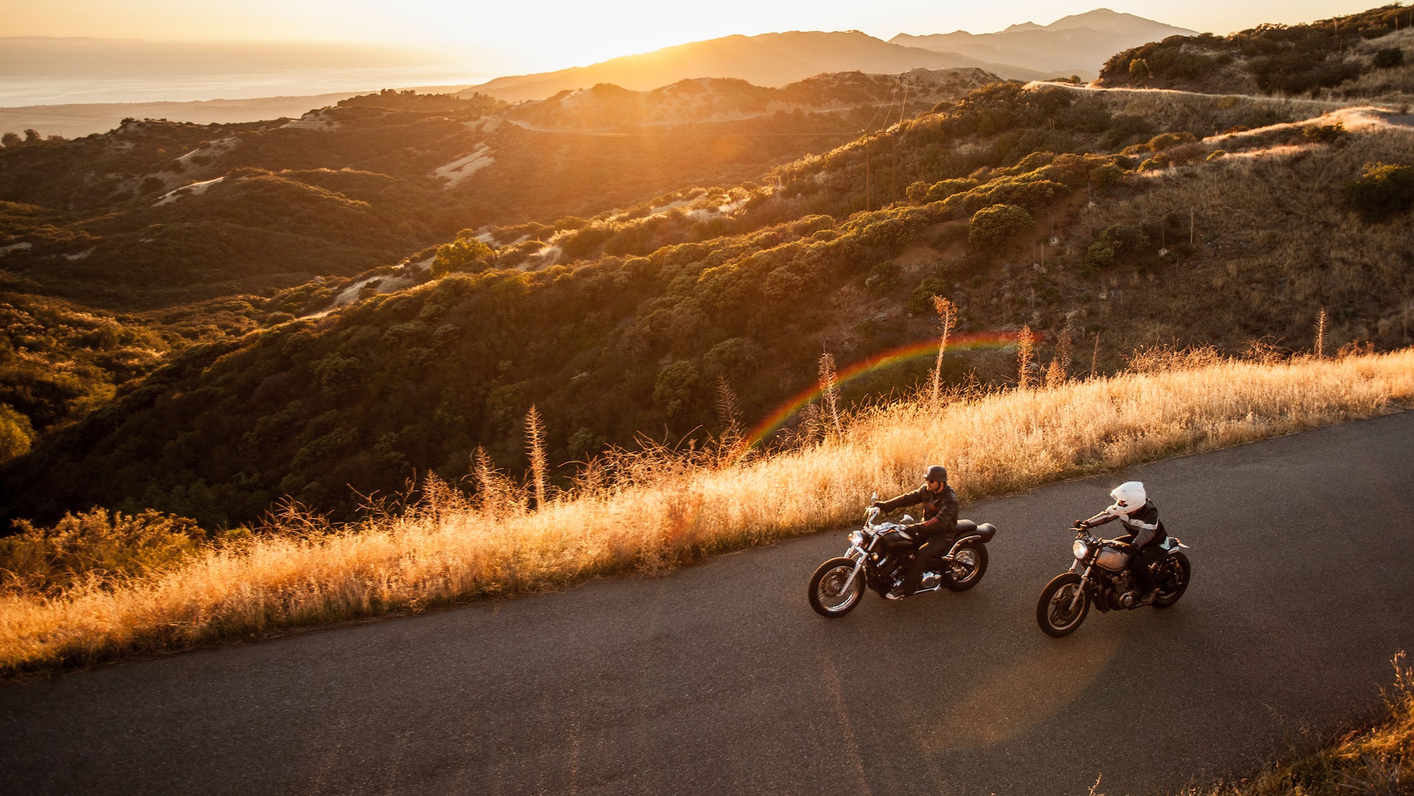 Zwei Motorräder fahren bei Sonnenuntergang auf einer Straße.