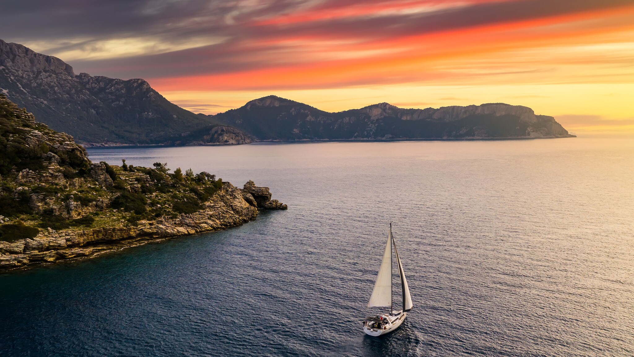 Ein Segelboot segelt auf einem Meer an einer Küste entlang.