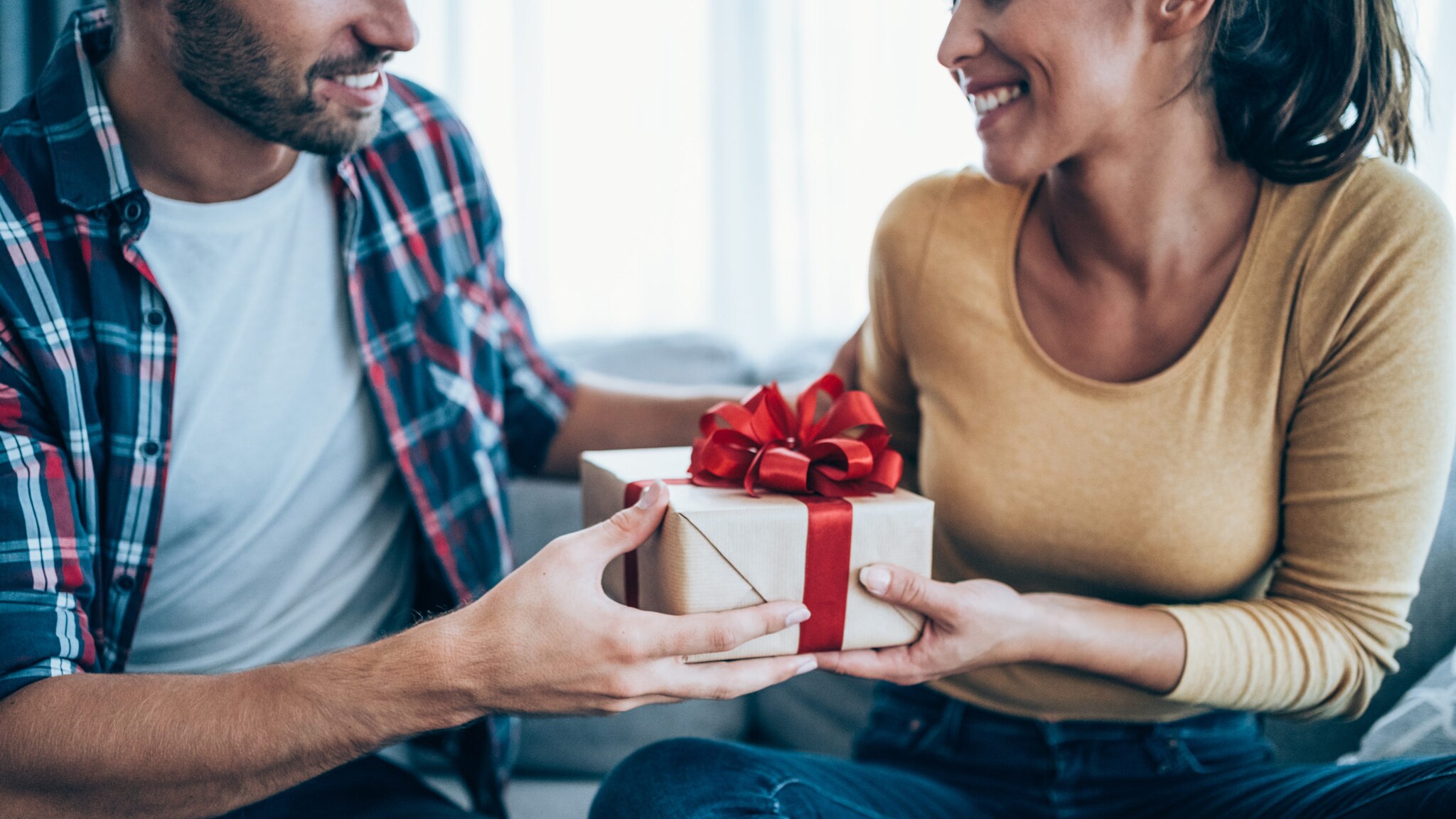 Ein Mann überreicht einer sich freuenden Frau ein Geschenk mit roten Schleife.