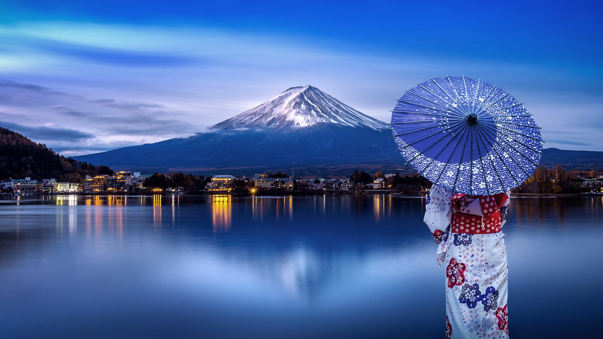 Frau in traditionell-japanischem Kimono mit Schirm blickt auf den schneebedeckten Fuji-Berg.