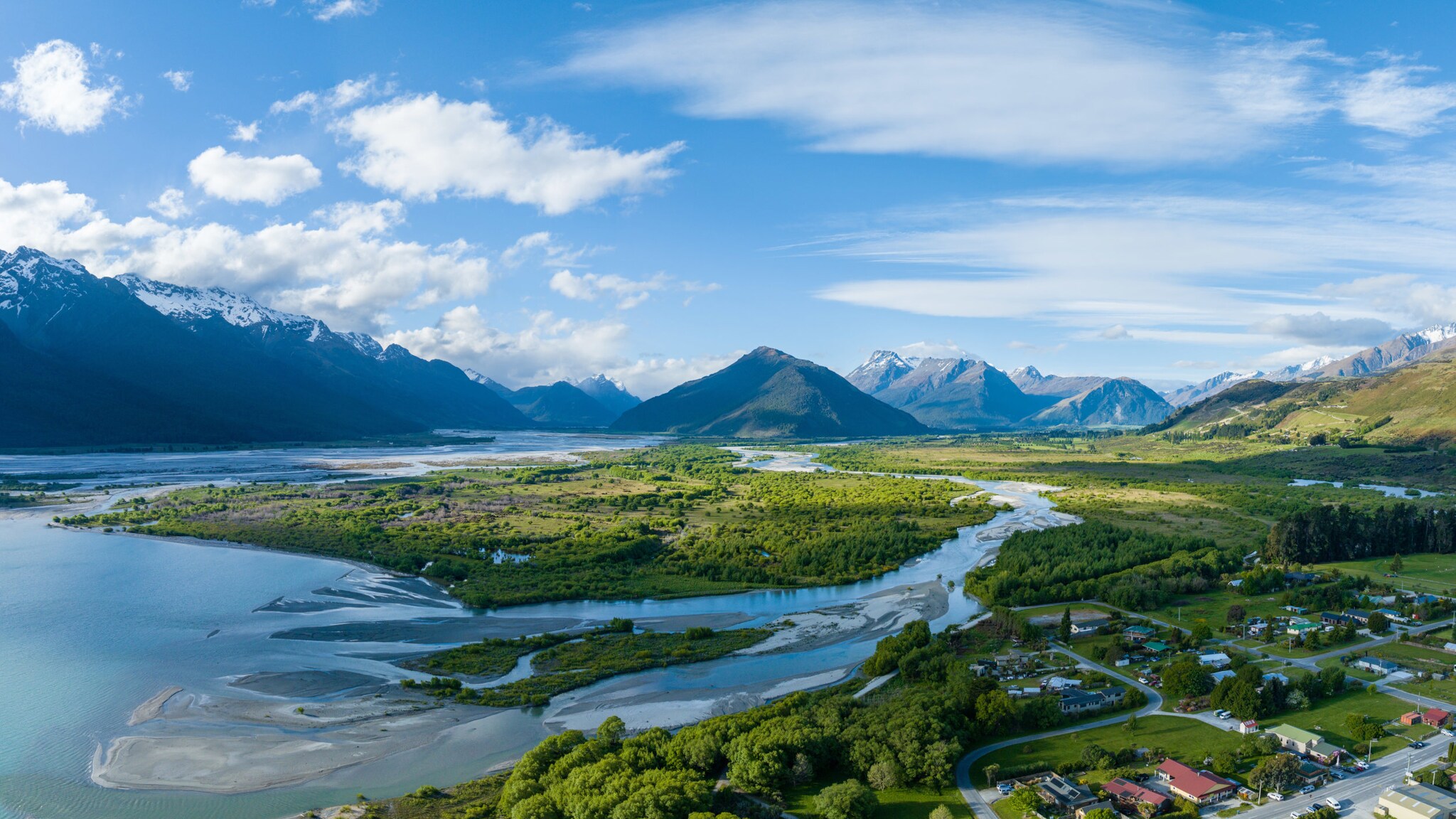 Das am Wasser liegende neuseeländische Dorf Glenorchy von oben, umgeben von grüner Landschaft und imposanten Bergen.