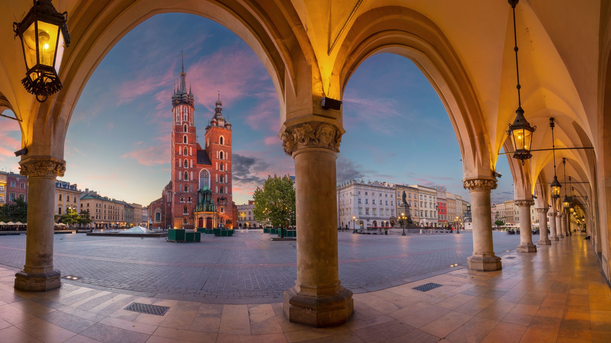 Blick durch Arkaden hinweg auf den Krakauer Marktplatz bei Sonnenaufgang.