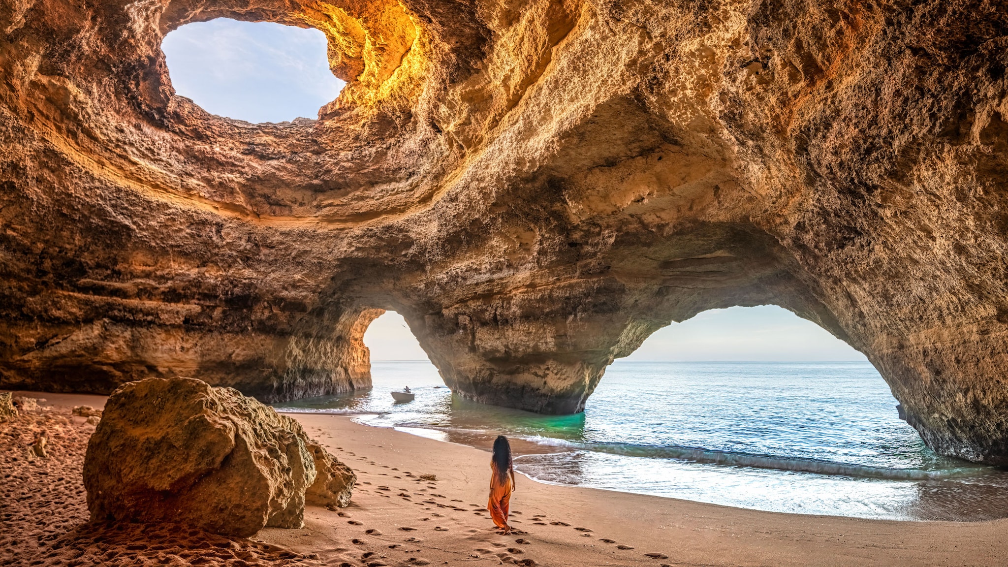 Frau spaziert durch die faszinierende Benagil-Höhle an der Algarve in Portugal und blickt auf das offene Meer.