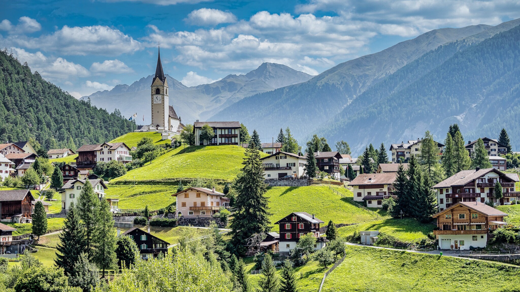 Idyllisches Bergdorf mit traditionellen Häusern und einer Kirche zwischen grünen Wiesen und satten Tannenwäldern.