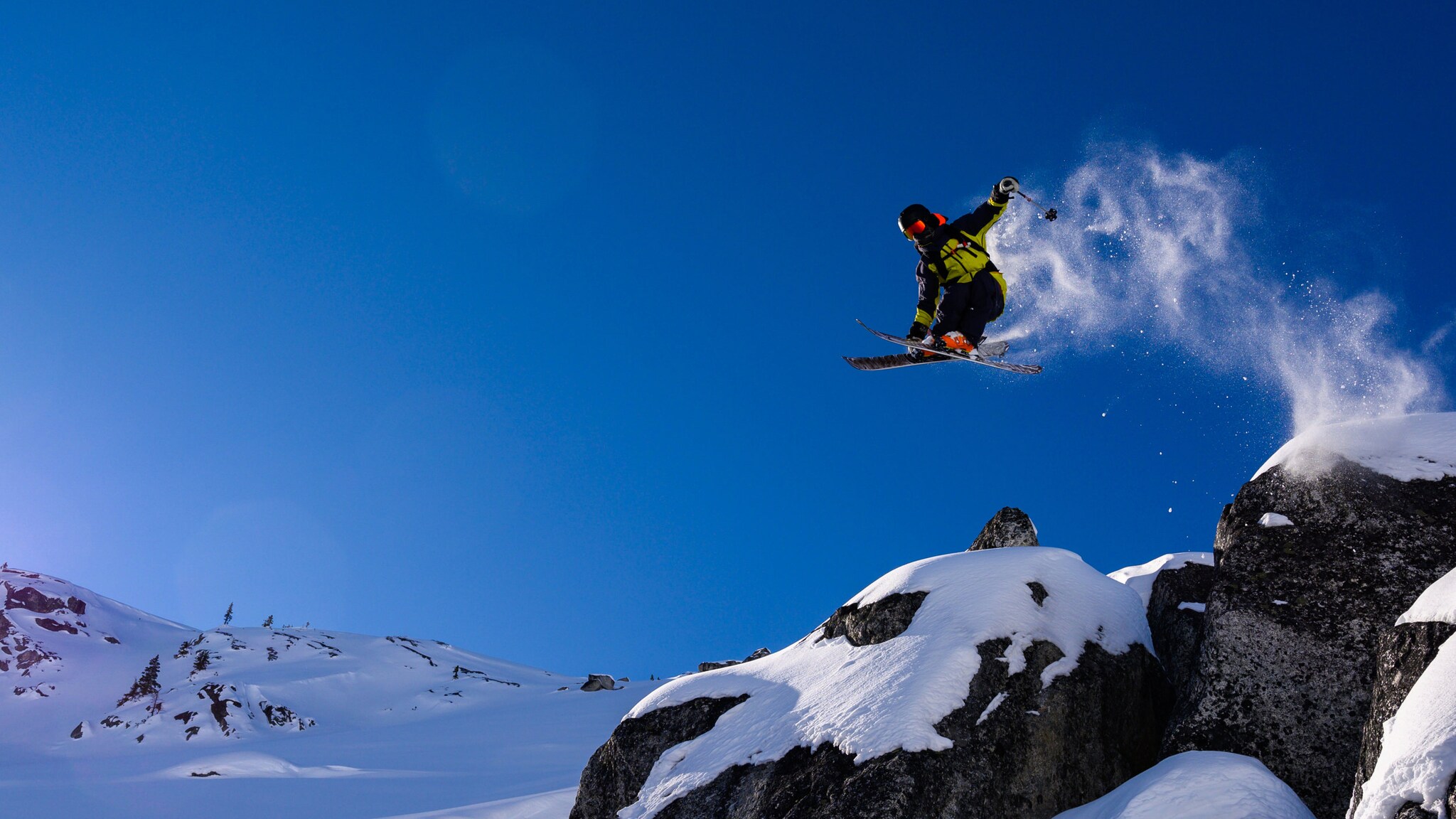 Ein Ski-Freerider bei blauem Himmel in der Luft, unter ihm ist eine weiße Schneelandschaft.