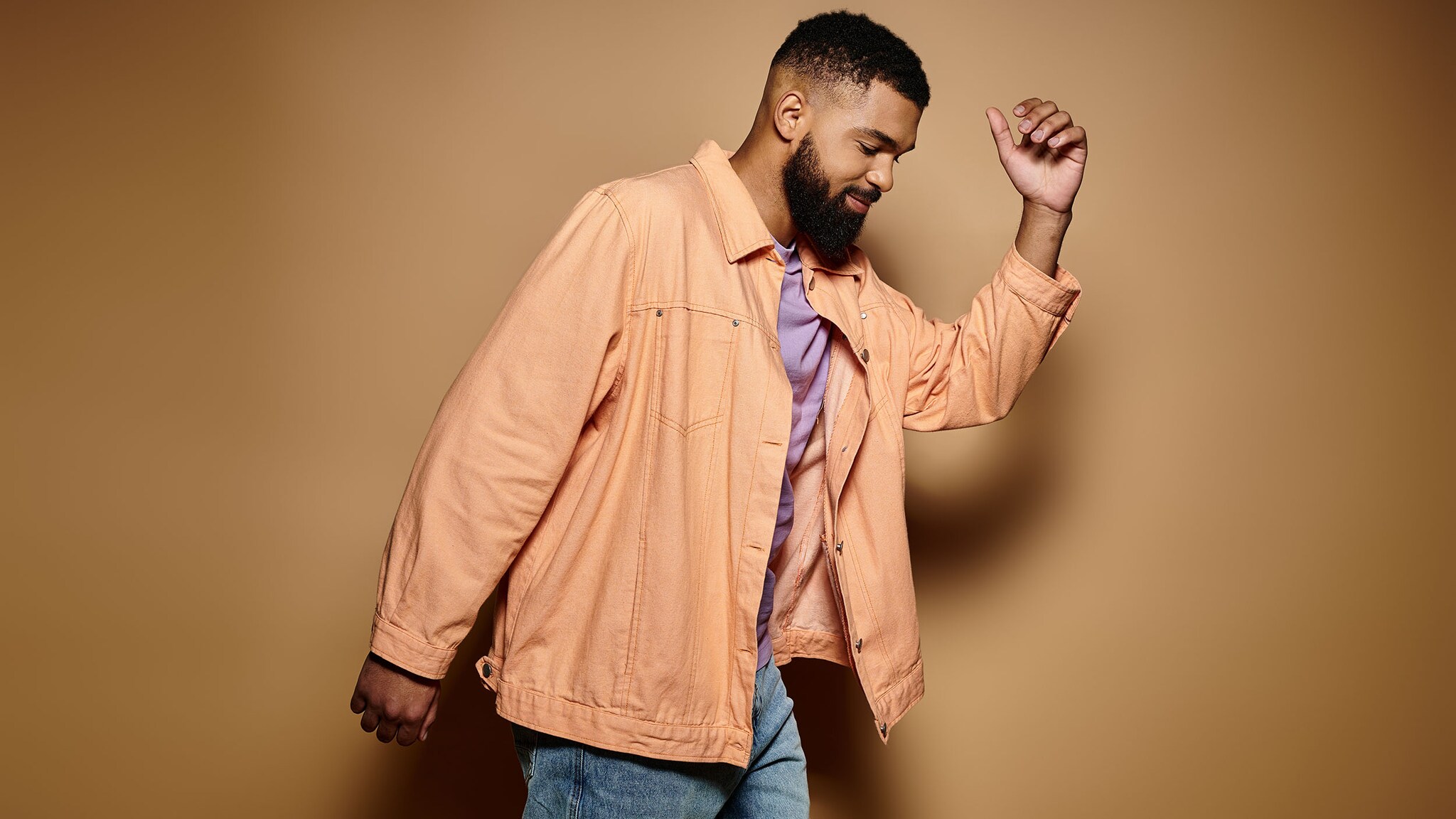 Ein Mann in modischer Kleidung posiert vor einer beigen Wand.