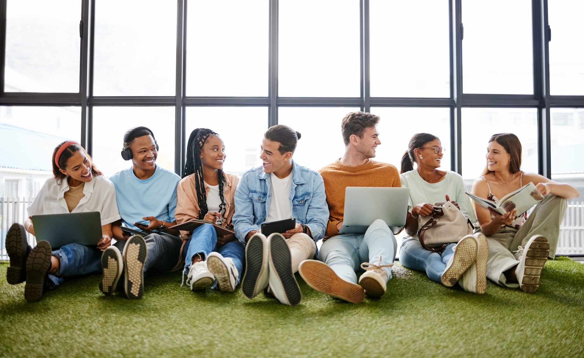 Mehrere junge Personen sitzen nebeneinander auf dem Fußboden an eine Fensterfront gelehnt. Mehrere junge Personen sitzen nebeneinander auf dem Fußboden an eine Fensterfront gelehnt.