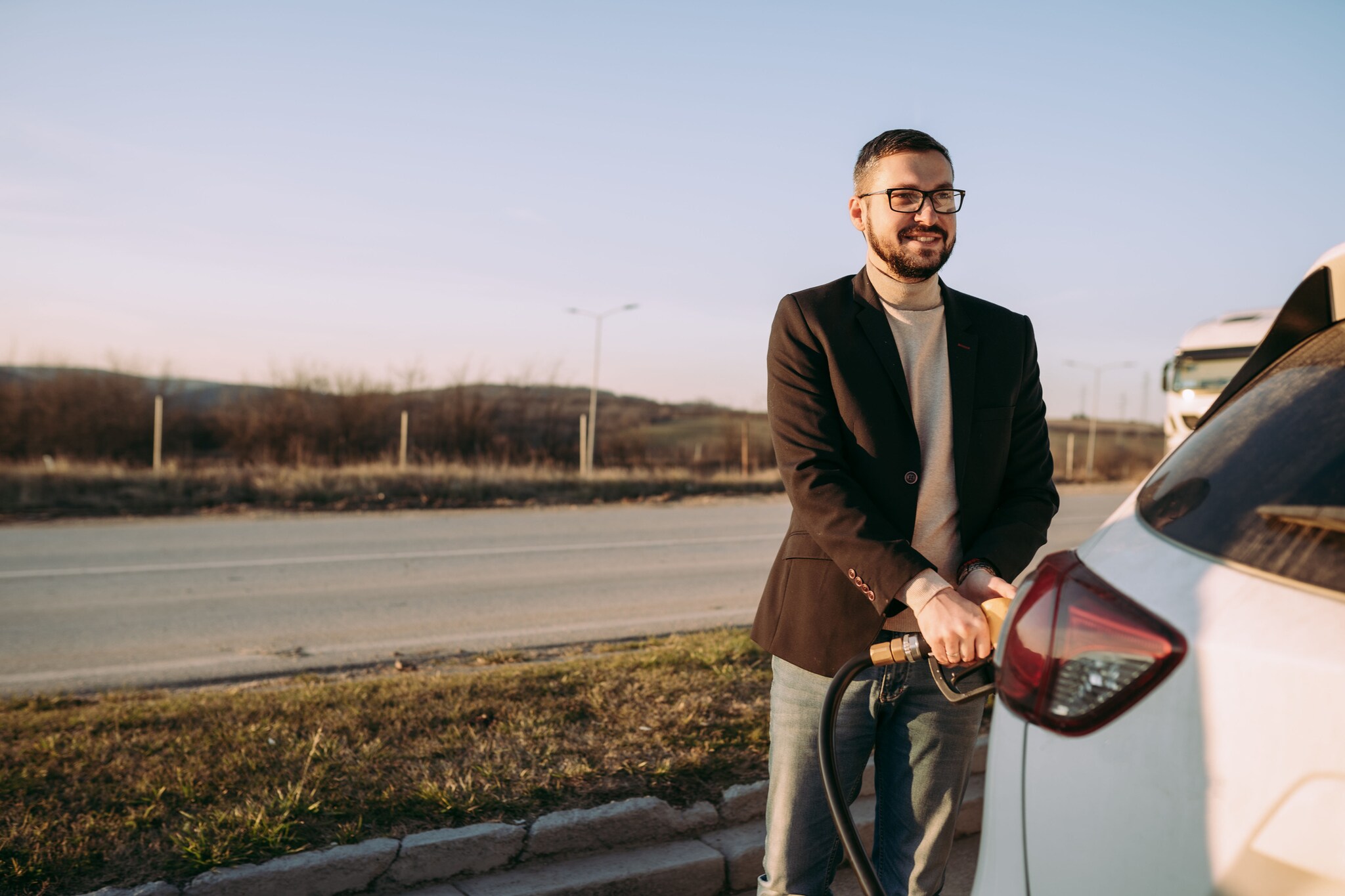 Eine Person steht vor ihrem Auto und hält den Zapfhahn fest, der im Auto steckt. Eine Person steht vor ihrem Auto und hält den Zapfhahn fest, der im Auto steckt.