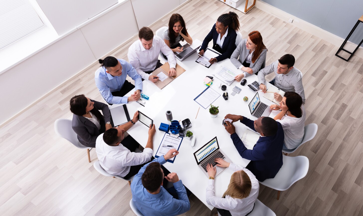Eine Gruppe von zwölf Personen sitzt mit Laptops an einem Tisch. Eine Gruppe von zwölf Personen sitzt mit Laptops an einem Tisch.