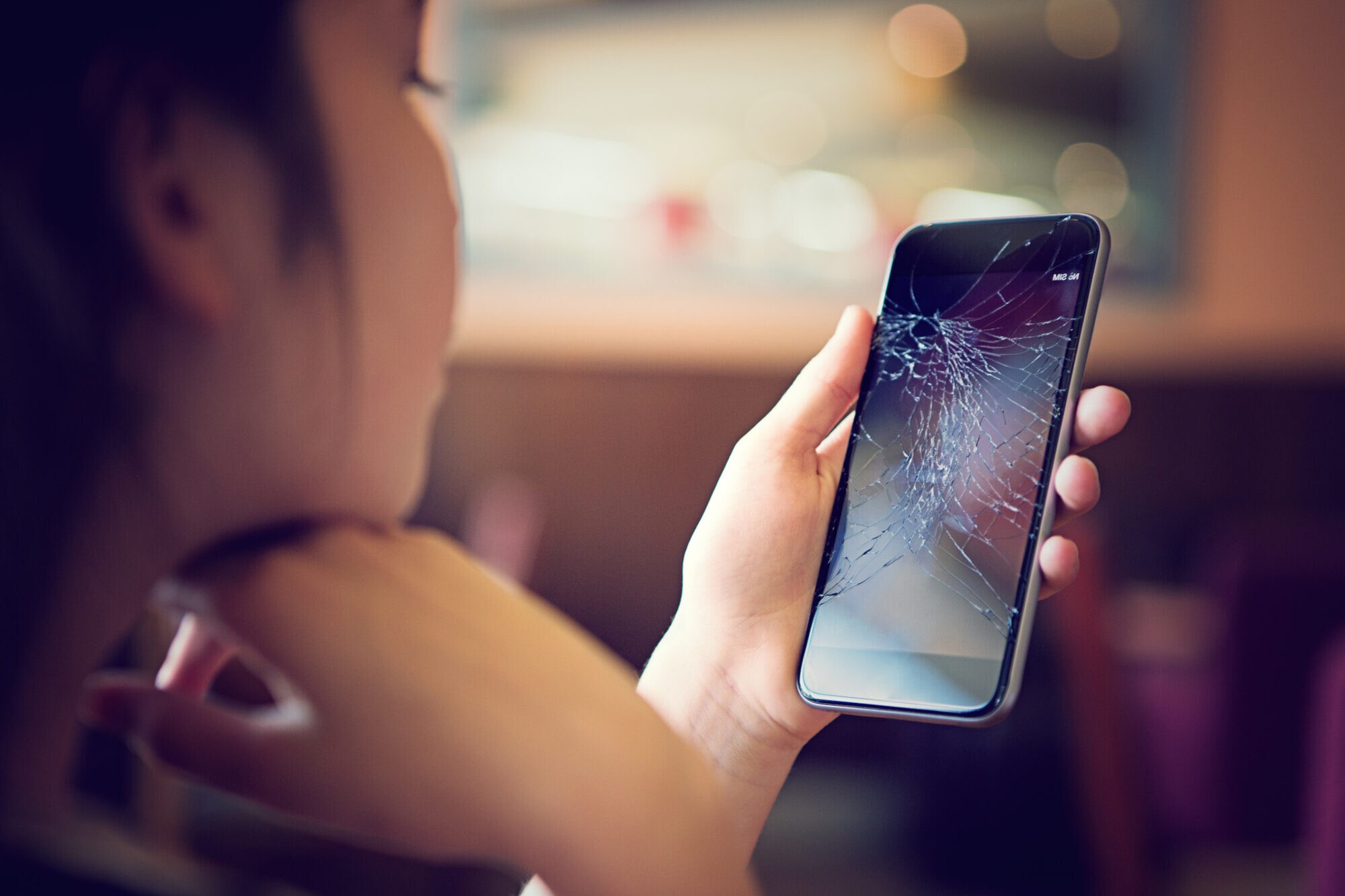 Eine Person betrachtet das Display ihres Smartphones, das zersprungen ist.