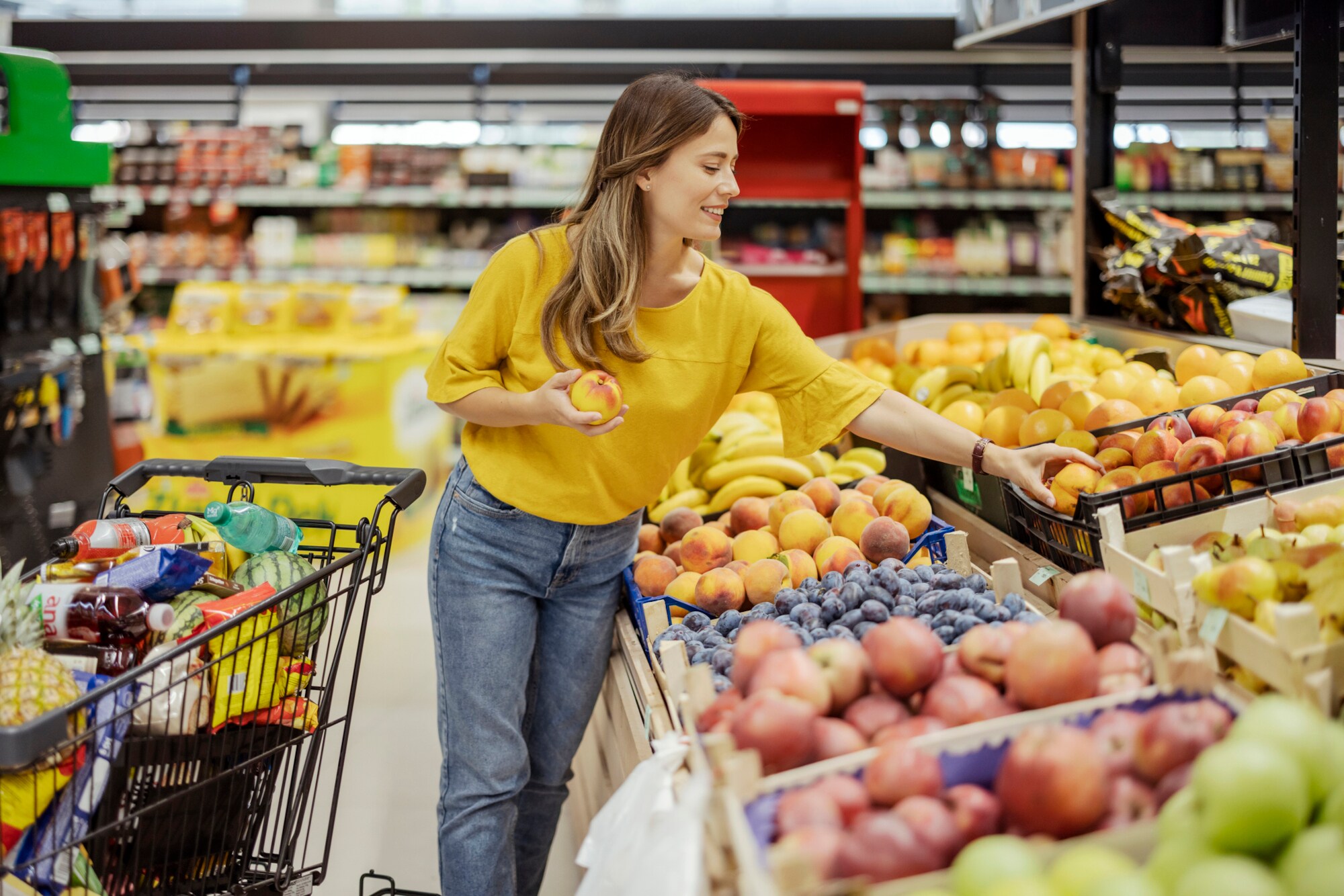 Eine Person greift im Supermarkt nach Pfirsichen.