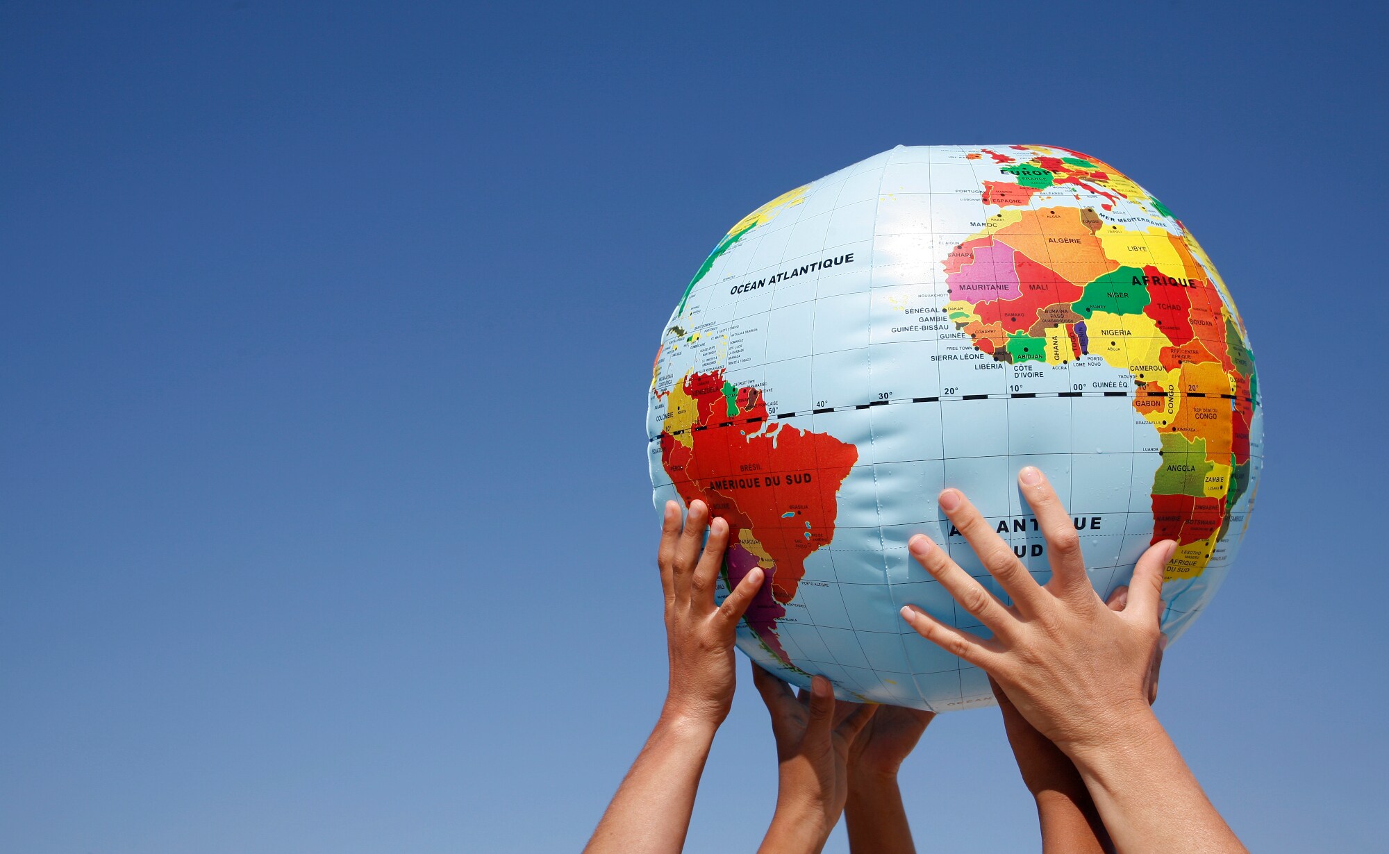 Mehrere Hände halten einen Ball mit Weltkugelmotiv in die Höhe.