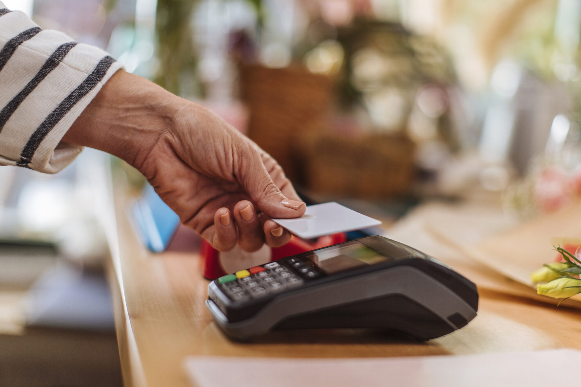 Eine Person hält eine Karte zum Bezahlen an ein Kartenlesegerät.