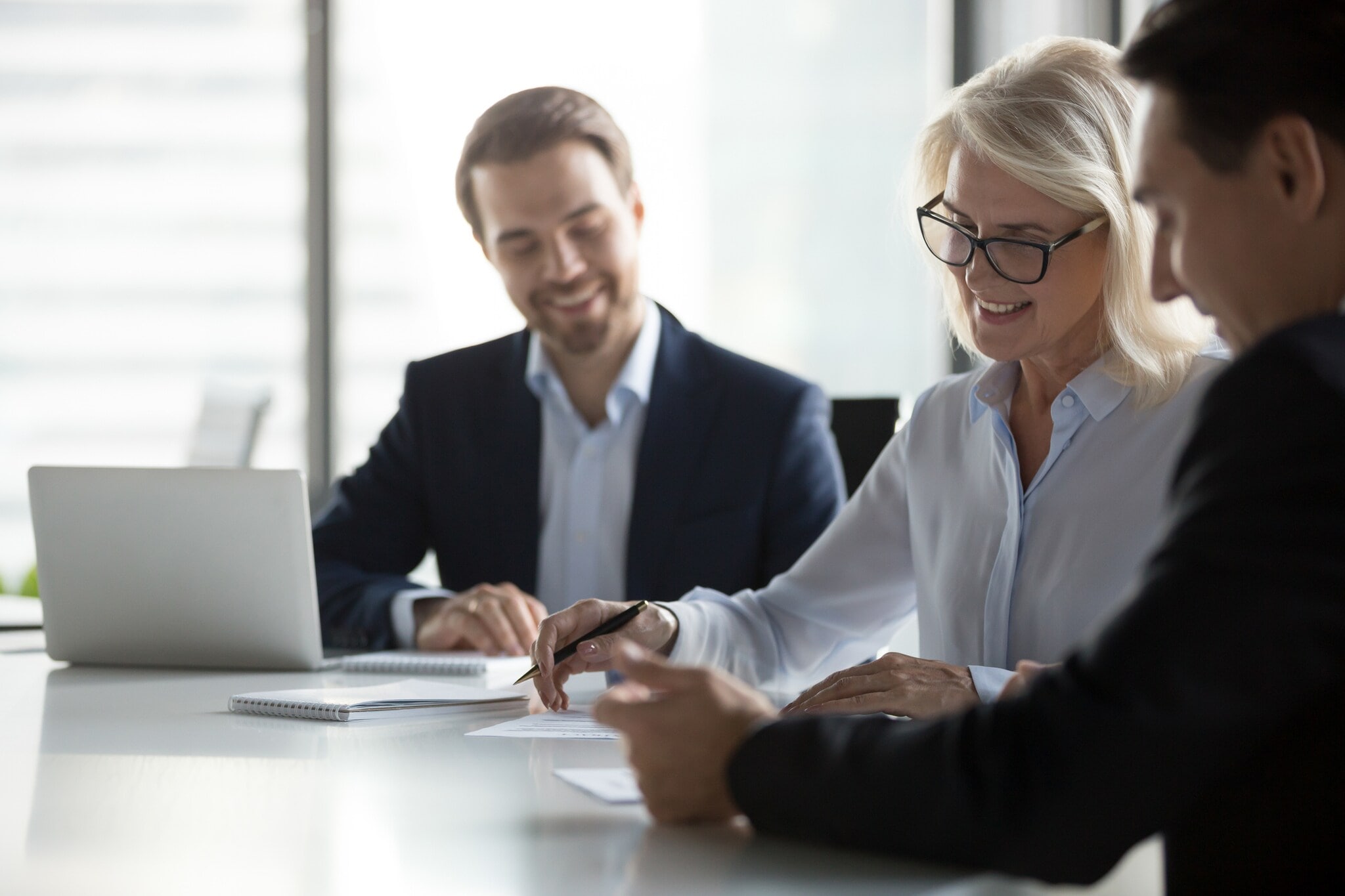 Drei Personen in Businesskleidung sitzen an einem Tisch, auf dem sich ein aufgeklappter Laptop und Papierunterlagen befinden. Drei Personen in Businesskleidung sitzen an einem Tisch, auf dem sich ein aufgeklappter Laptop und Papierunterlagen befinden.