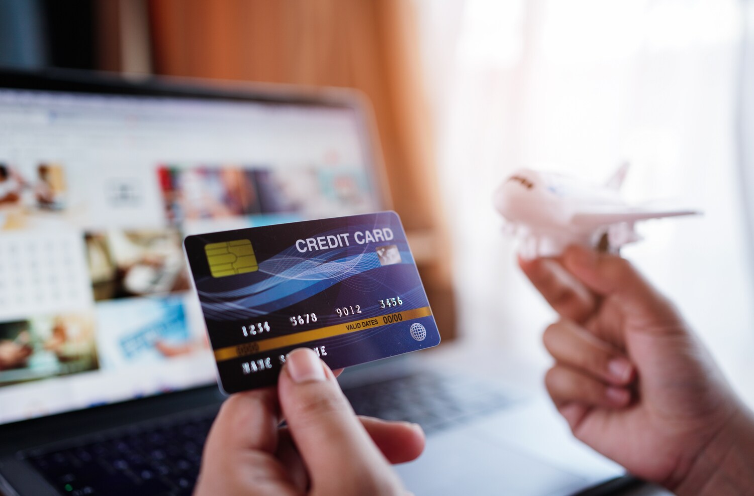 Zwei Hände, eine Kreditkarte und ein Flugzeugmodell haltend, vor einem Laptopbildschirm