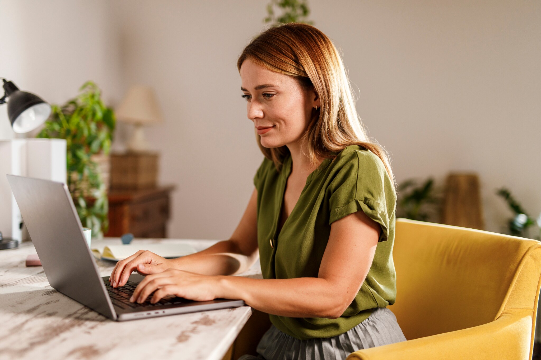 Name Eine Frau sitzt an einem Tisch vor einem Laptop und legt ihre Hände auf die Tastatur.