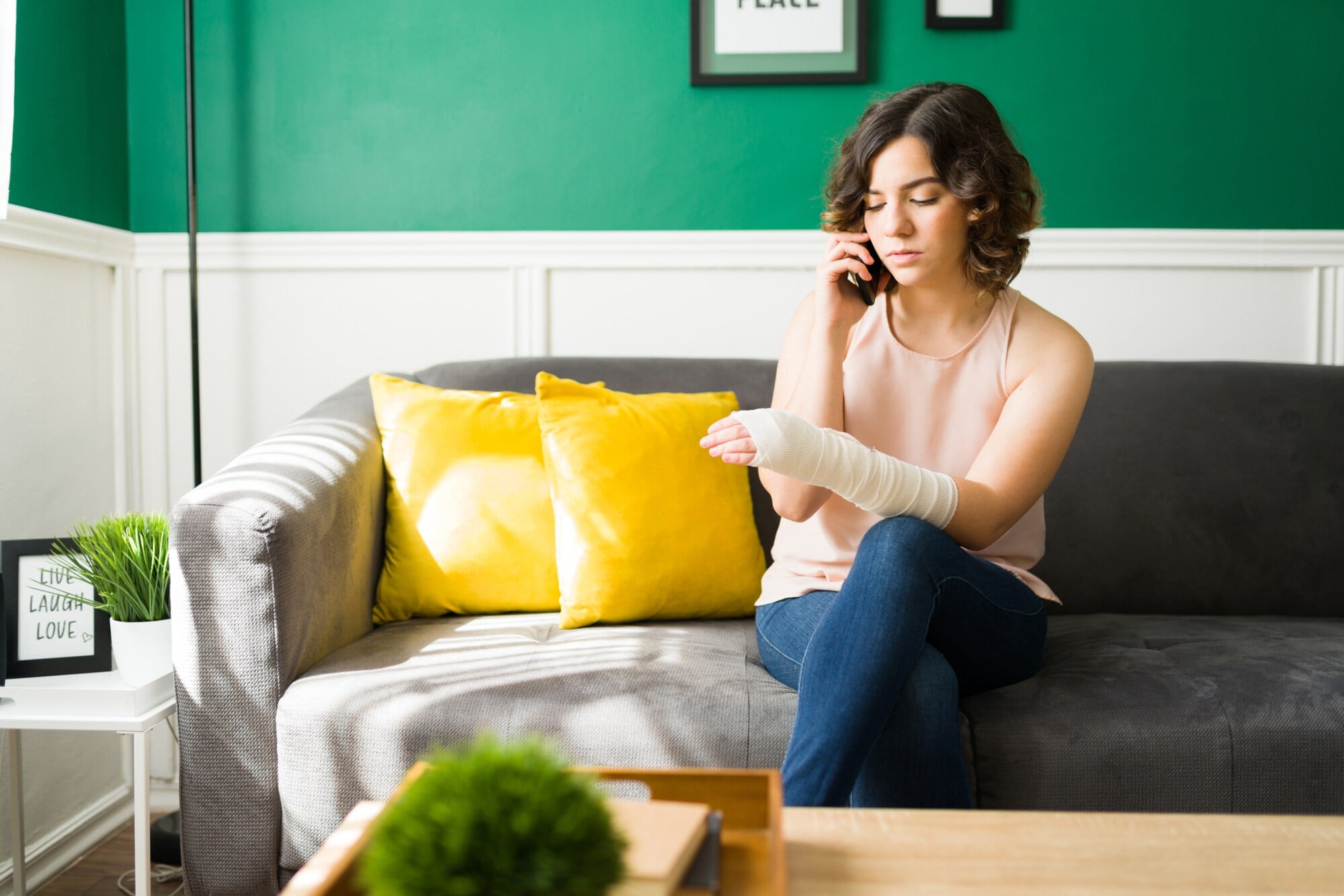 Eine Person sitzt mit einbandagiertem Arm auf einem Sofa und telefoniert. Eine Person sitzt mit einbandagiertem Arm auf einem Sofa und telefoniert.