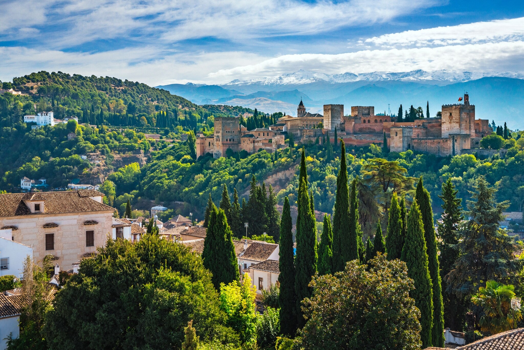 Blick auf einzelne Häuser und die von Wald umgebene Alhambra, im Hintergrund Berge. Blick auf einzelne Häuser und die von Wald umgebene Alhambra, im Hintergrund Berge.