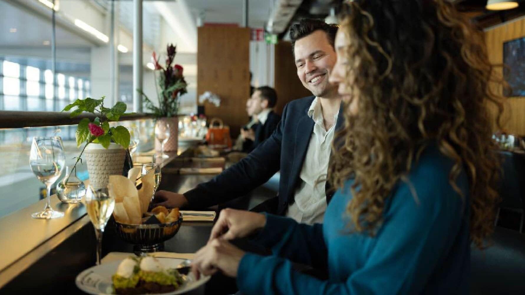 Ein Mann und eine Frau beim Essen an einem Fensterplatz in einer Flughafen-Lounge. Ein Mann und eine Frau beim Essen an einem Fensterplatz in einer Flughafen-Lounge.