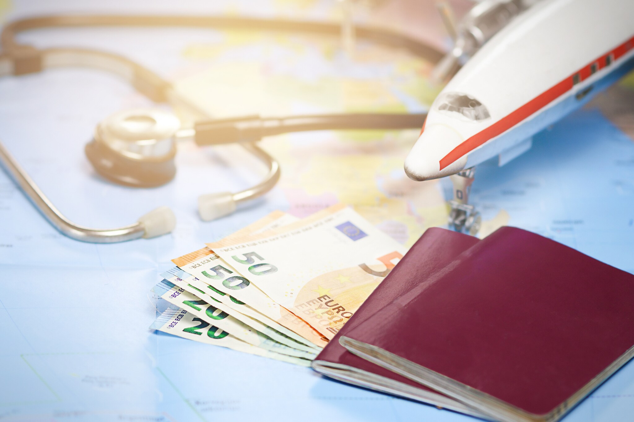 GettyImages-1305908661 Artikelbild Weltkarte mit Geldscheinen, Reisepass, kleinem Flugzeug und Stethoskop