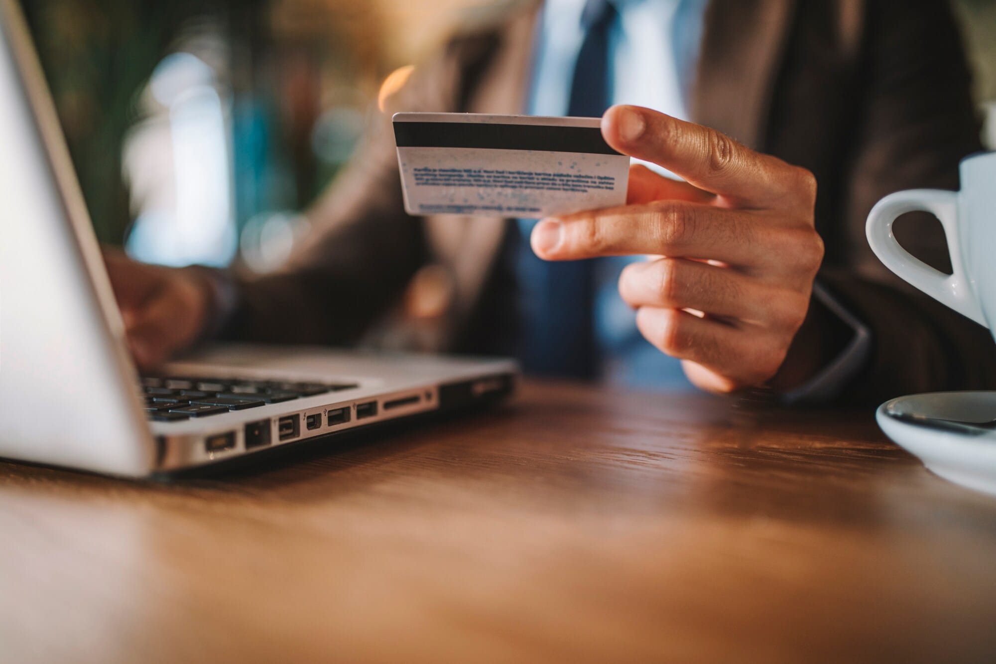 Nahaufnahme einer Hand, die neben einem geöffneten Laptop eine Kreditkarte in der Hand hält. Nahaufnahme einer Hand, die neben einem geöffneten Laptop eine Kreditkarte in der Hand hält.