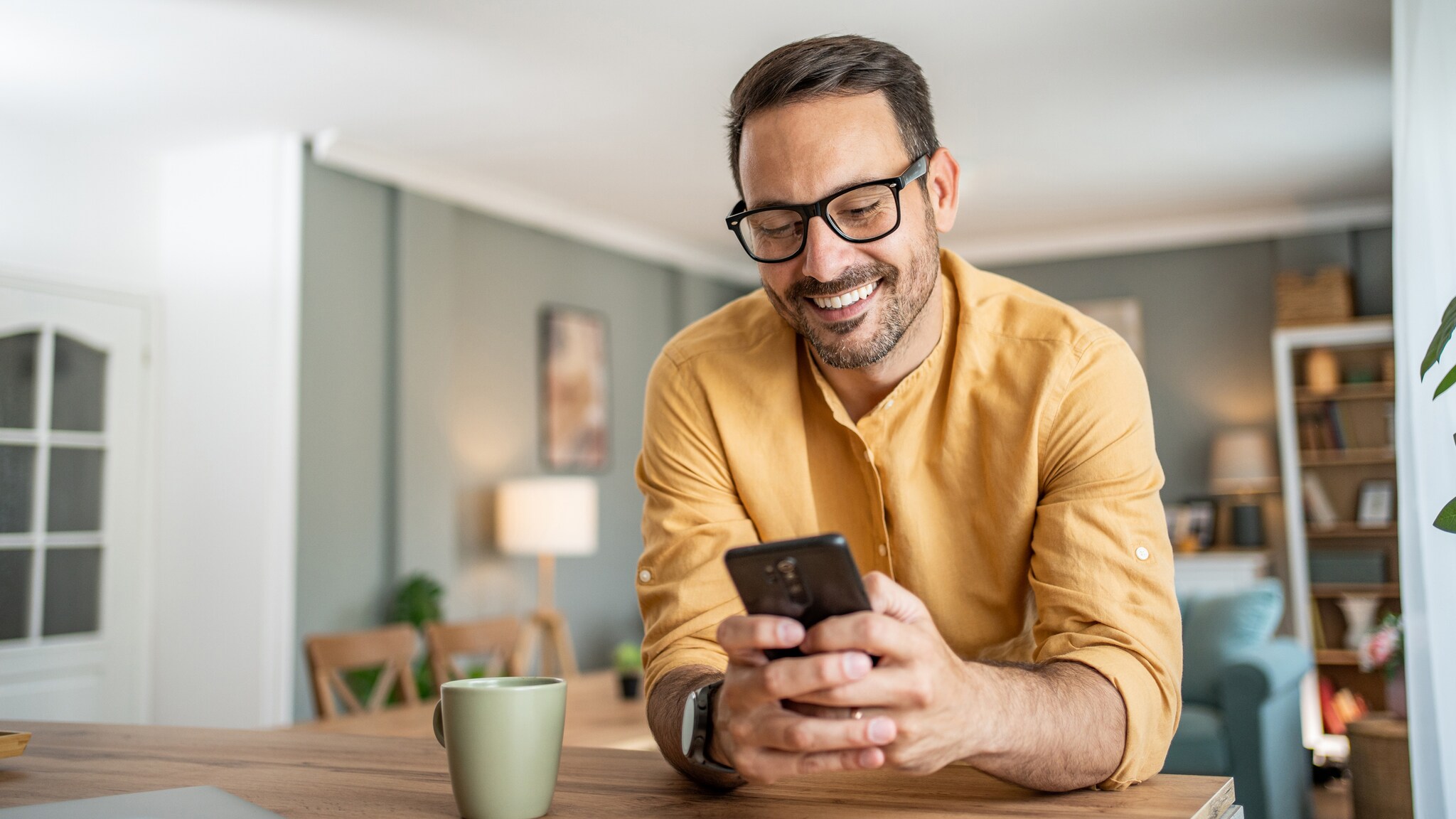 Eine Person lehnt auf einer Kücheninsel und blickt lächelnd auf das Smartphone in ihren Händen.