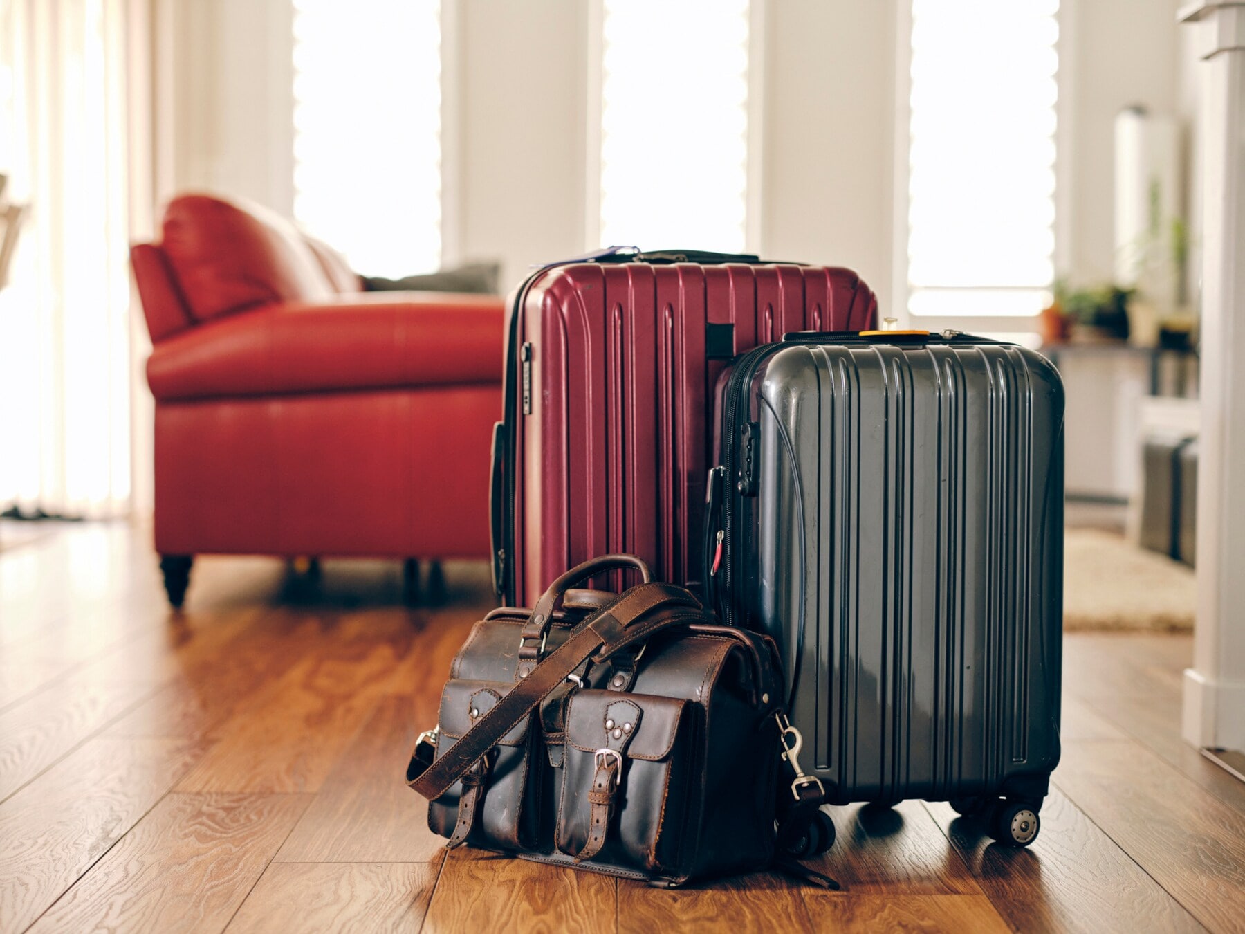 Zwei Koffer und eine Reisetasche stehen vor einem roten Sofa Zwei Koffer und eine Reisetasche stehen vor einem roten Sofa