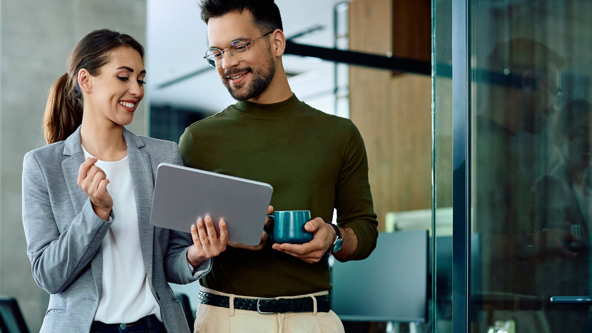 Eine Frau und ein Mann schauen in einem Büro stehend gemeinsam auf ein Tablet.