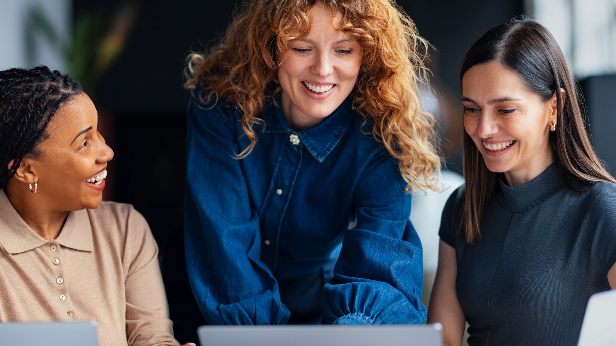 Drei Kolleginnen arbeiten gut gelaunt zusammen an einem Laptop in einem Büro.