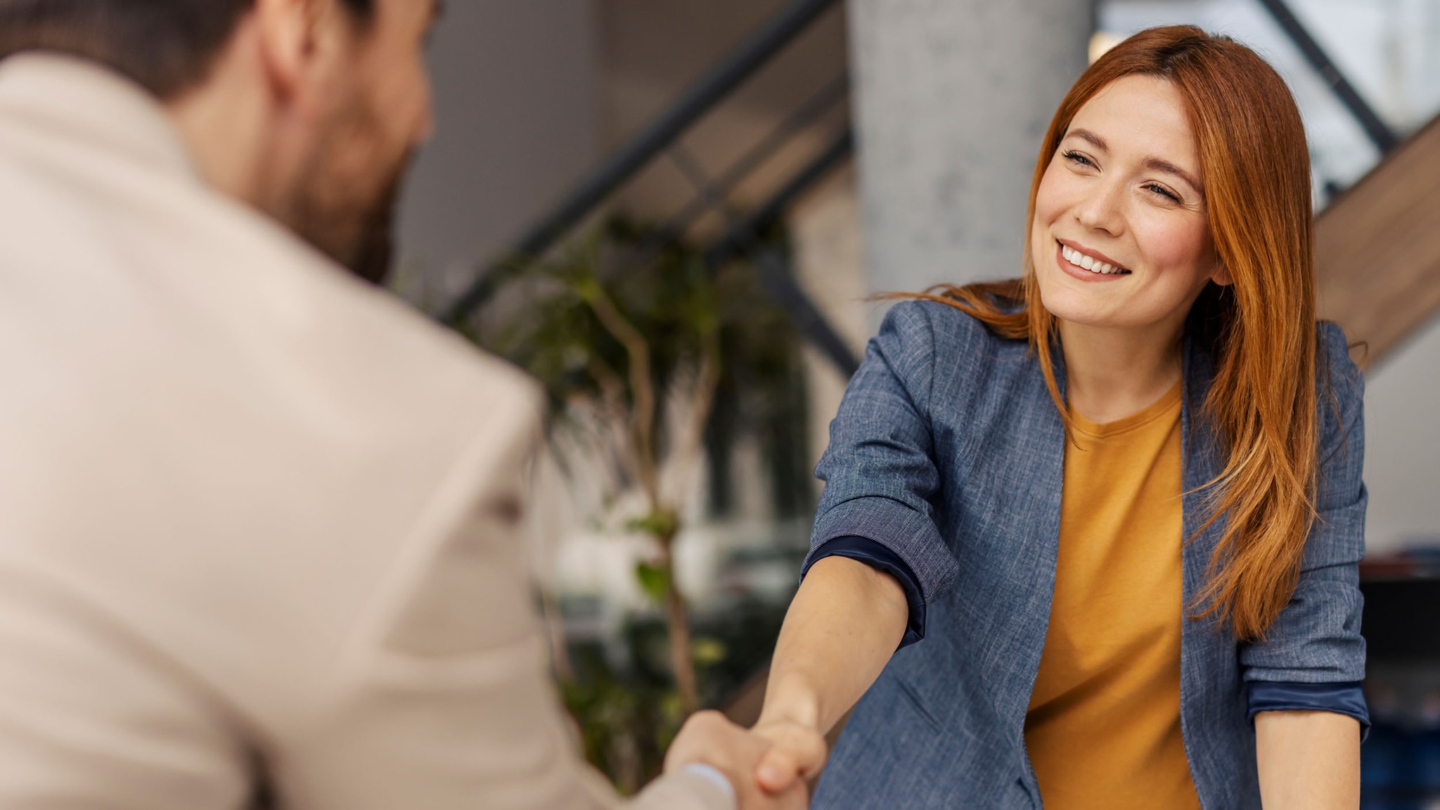 Eine lächelnde Frau und ein Mann in angeschnittener Rückansicht geben sich die Hand in einem Büro.