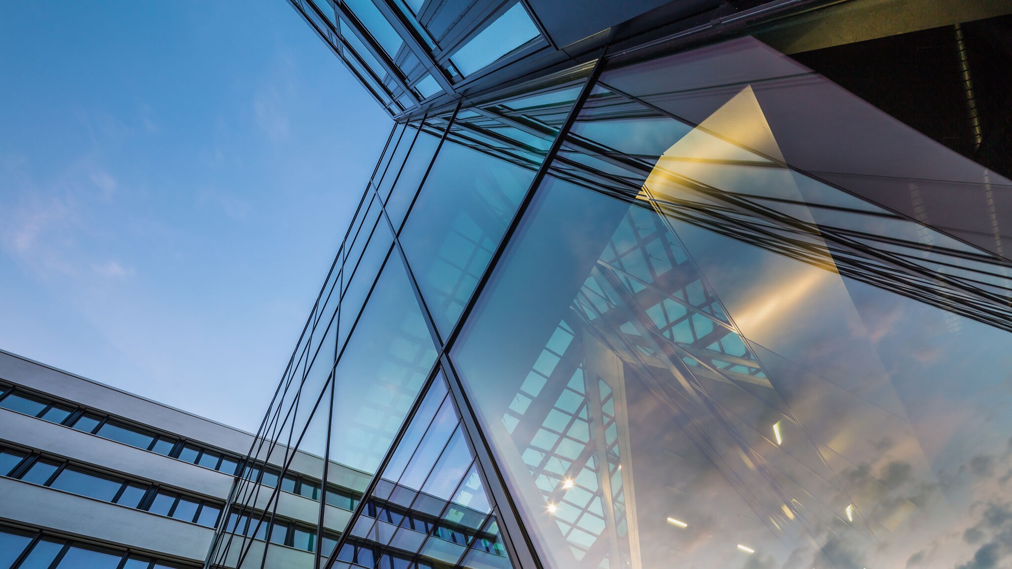 Glasfassade eines modernen Bürogebäudes unter blauem Himmel aus der Froschperspektive.