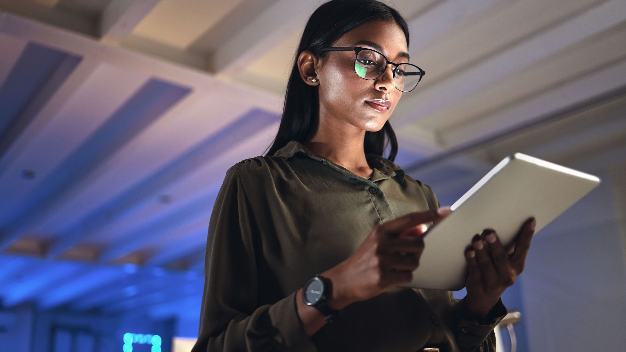 Eine junge Frau schaut stehend auf ein Tablet in ihren Händen in einem Serverraum mit blauem Licht.