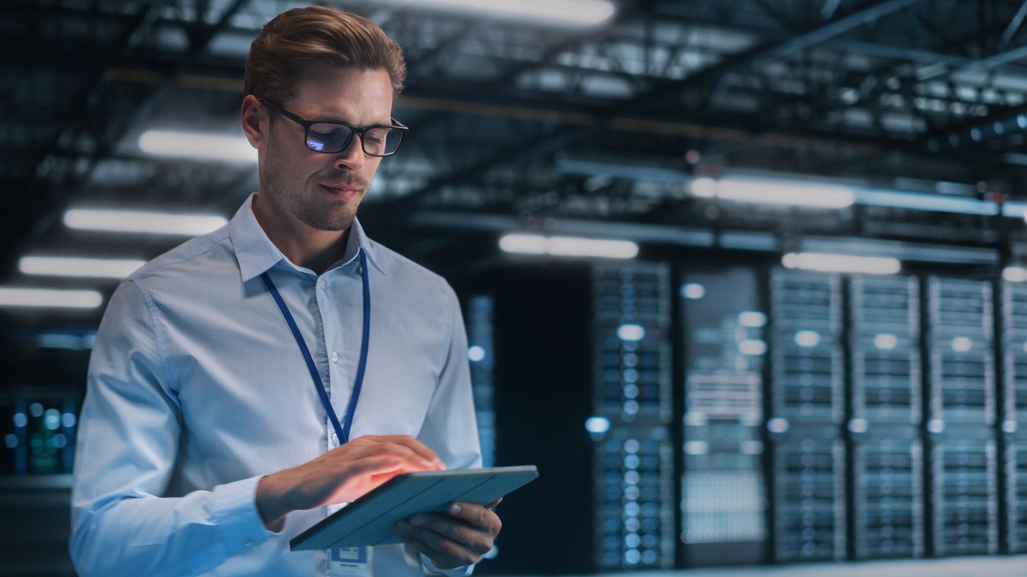 Ein Mann bedient stehend ein Tablet in seiner Hand in einem Serverraum.