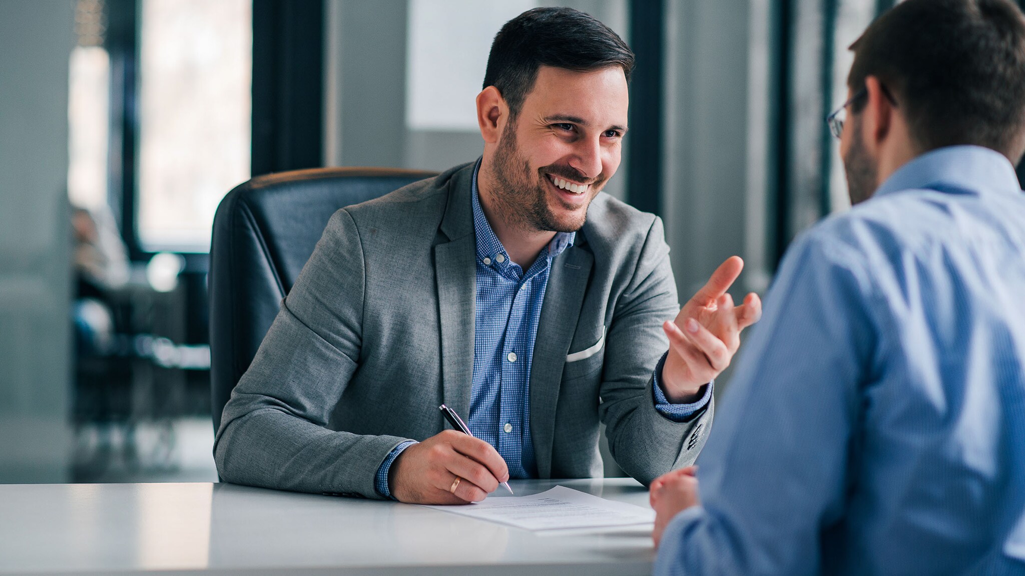 Zwei Männer in Businesskleidung sitzen sich gegenüber während eines Geschäftsmeetings an einem Schreibtisch in einem Büro.