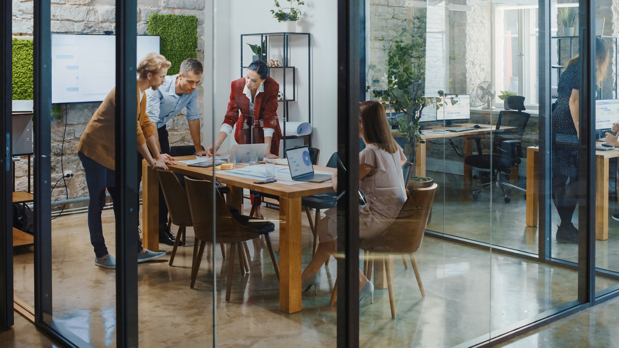 Personen stehen in einem Büro zusammen an einem Konferenztisch in einem Raum mit Glaswänden.