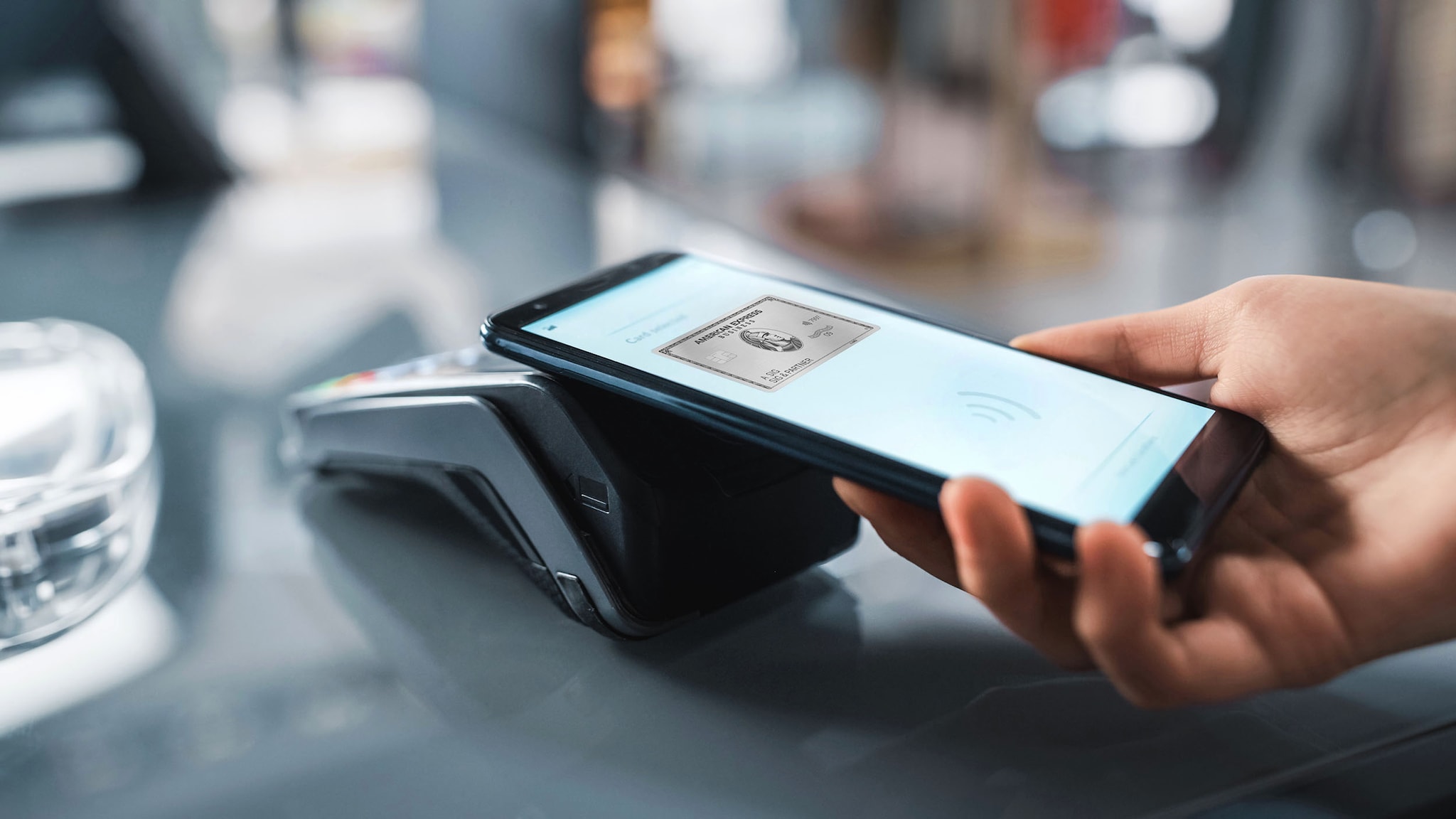 Kontaktlose Zahlung per Smartphone mit silberner Business Kreditkarte von American Express über ein Kartenlesegerät.