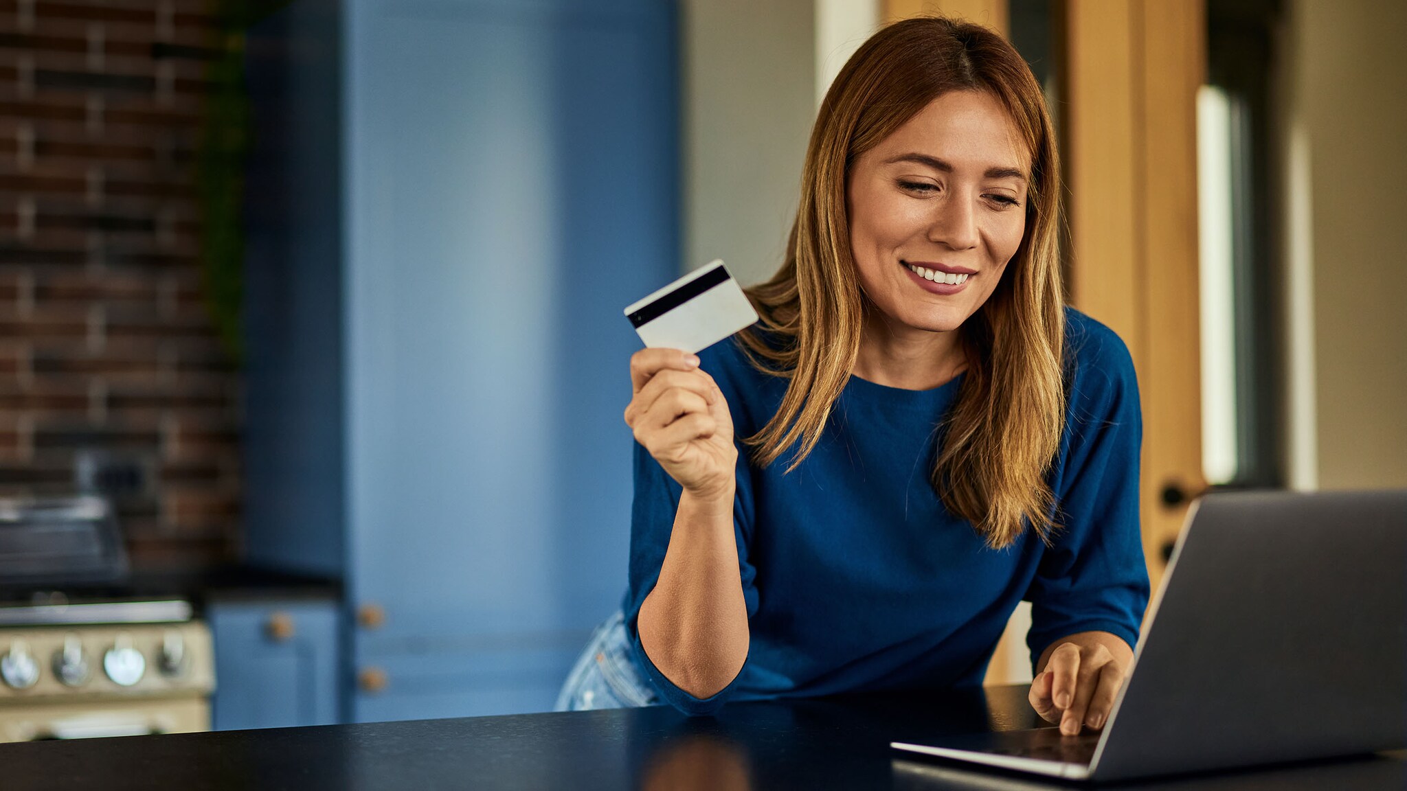 Eine Frau steht vor einem Laptop und hält eine Kreditkarte in der Hand.
