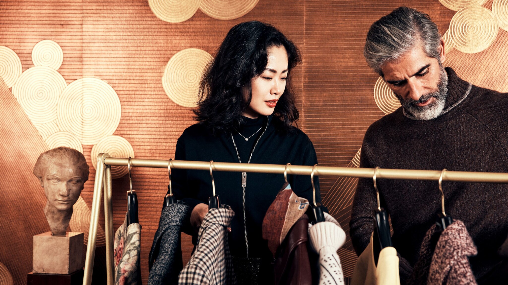 Personal Shopperin steht mit einem Kunden vor einer Kleiderstange.