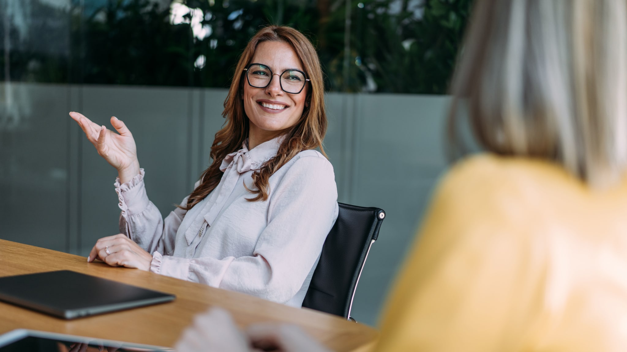 Eine Geschäftsfrau in Bluse kommuniziert selbstbewusst lächelnd an einem Konferenztisch in einem Büro.