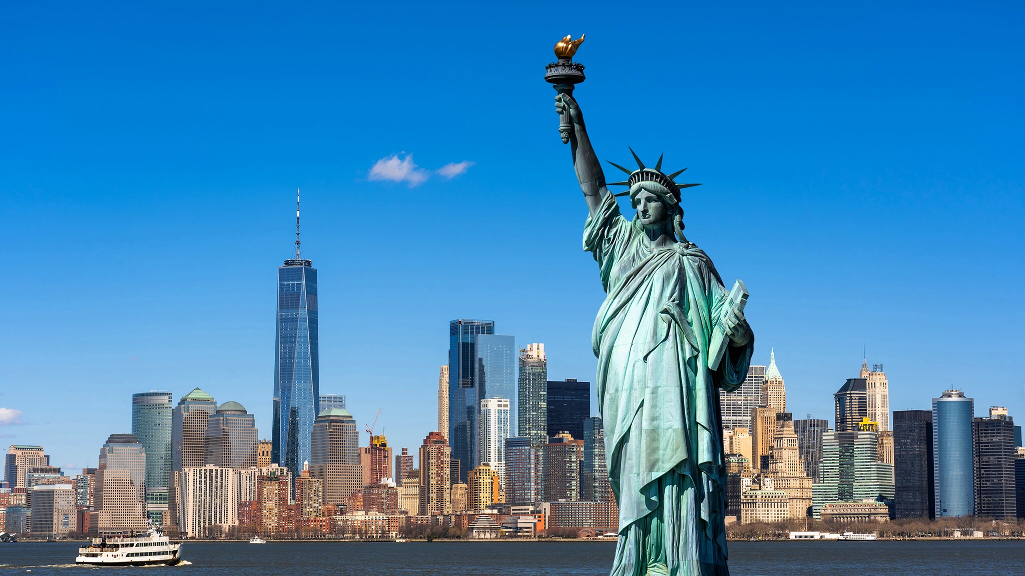 Eine grüne Skulptur mit Fackel in der Hand steht vor einer Skyline.